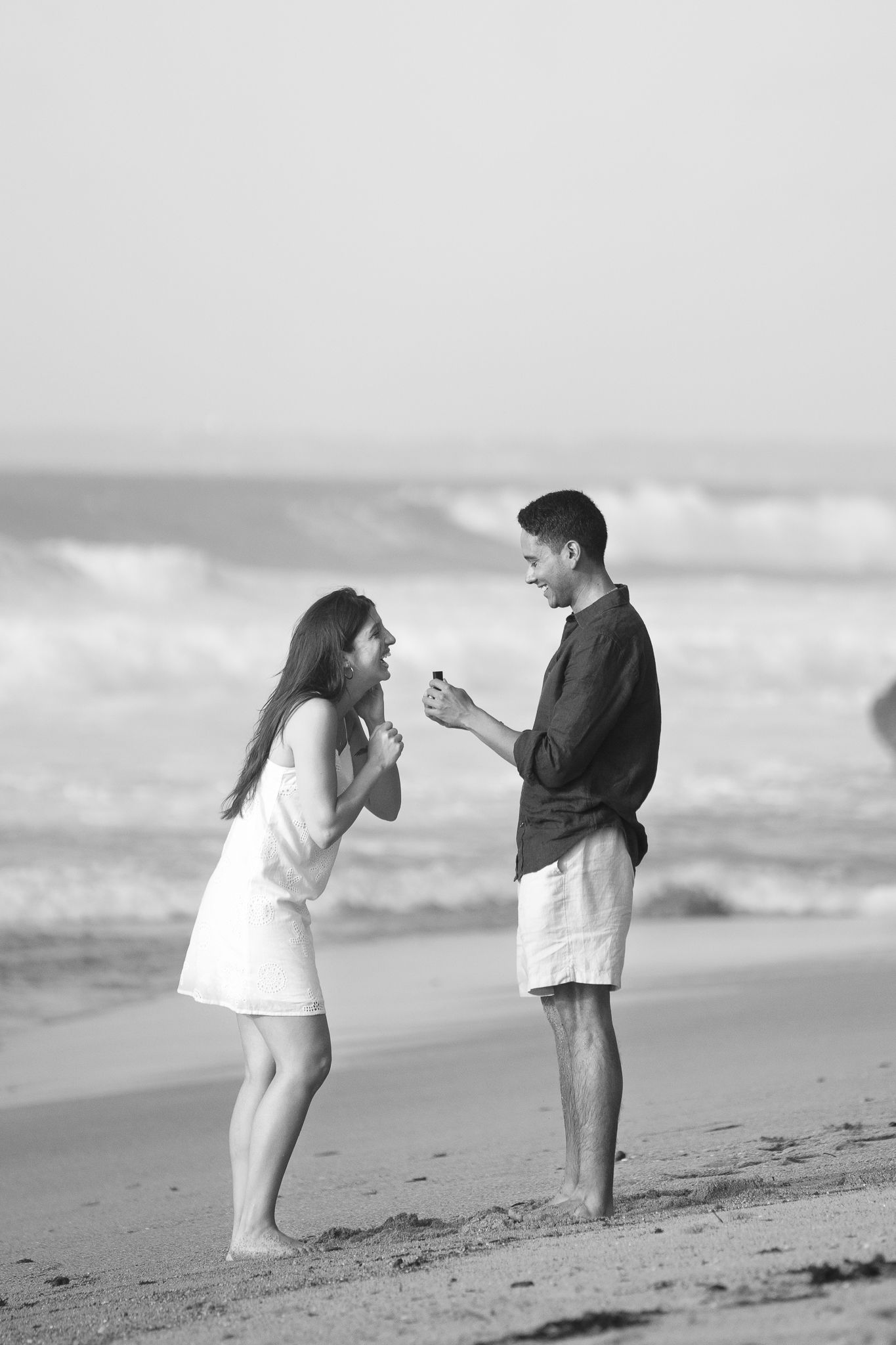 Black and white photo sequence showing two people interacting playfully on a beach with ocean waves in background.