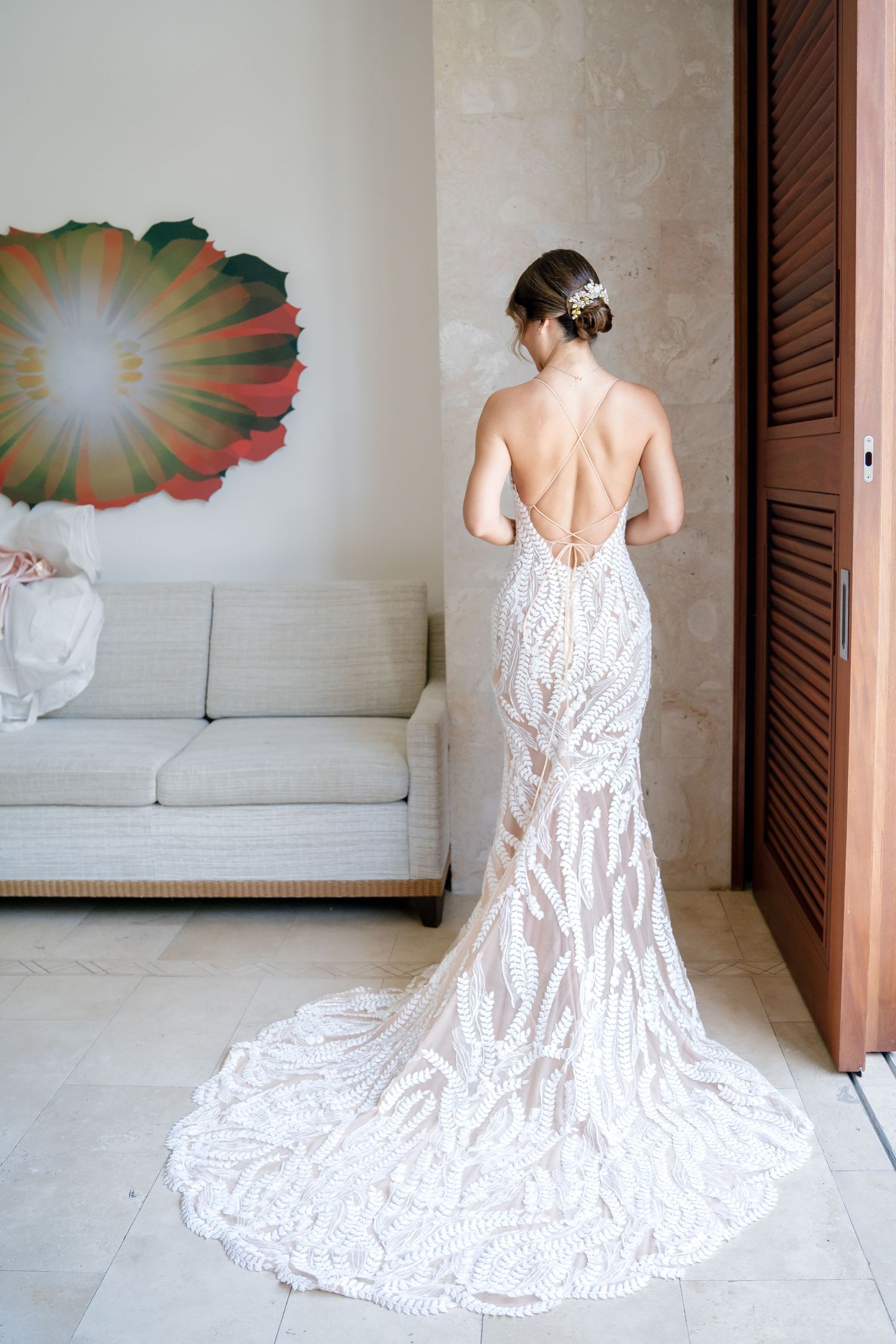 Back view of an elegant wedding gown with intricate lace details and dramatic train against neutral interior decor.