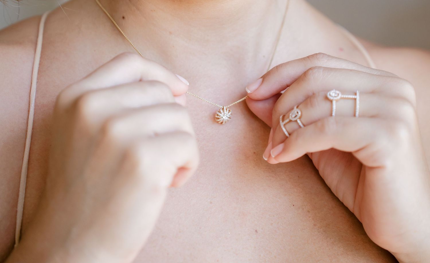 Close up shot of hands fastening a delicate necklace around a neck.