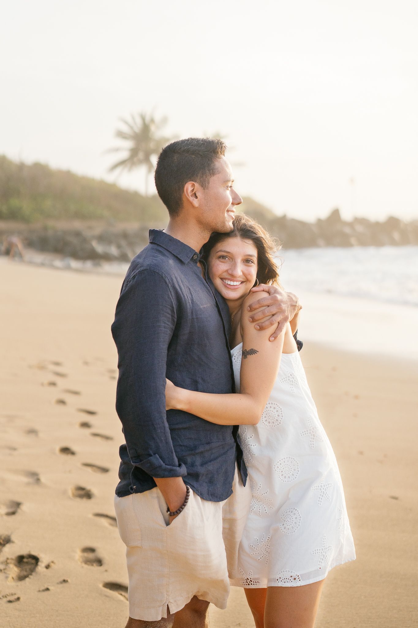A couple shares a romantic moment while embracing on a sandy beach at sunset.