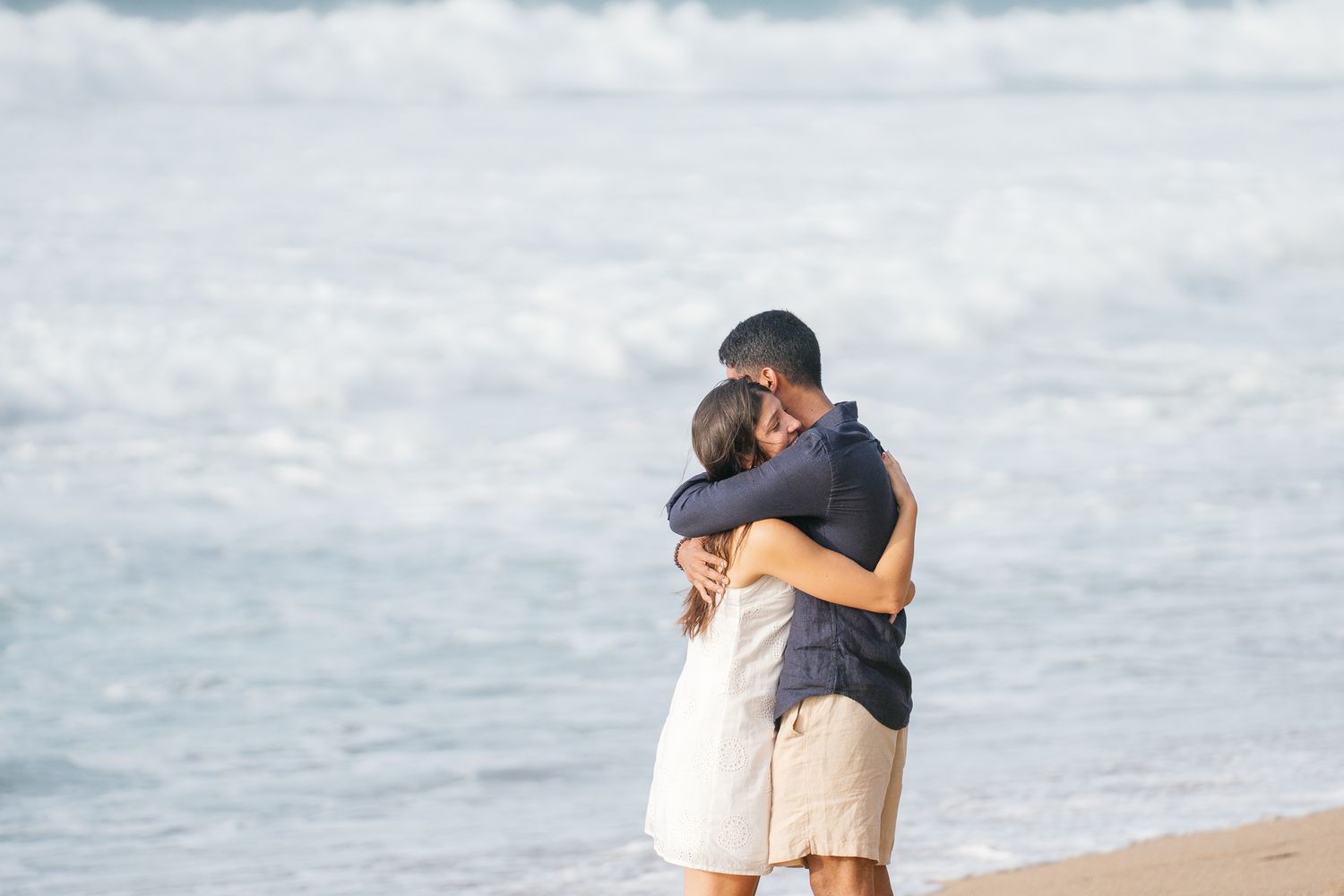 A couple shares a tender embrace while standing on a misty beach with cloudy skies in the background.
