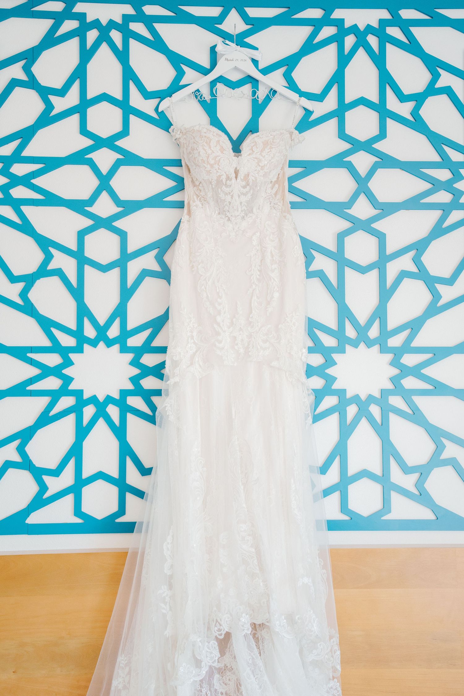 Elegant lace wedding dress hanging on a decorative blue and white geometric patterned wall.