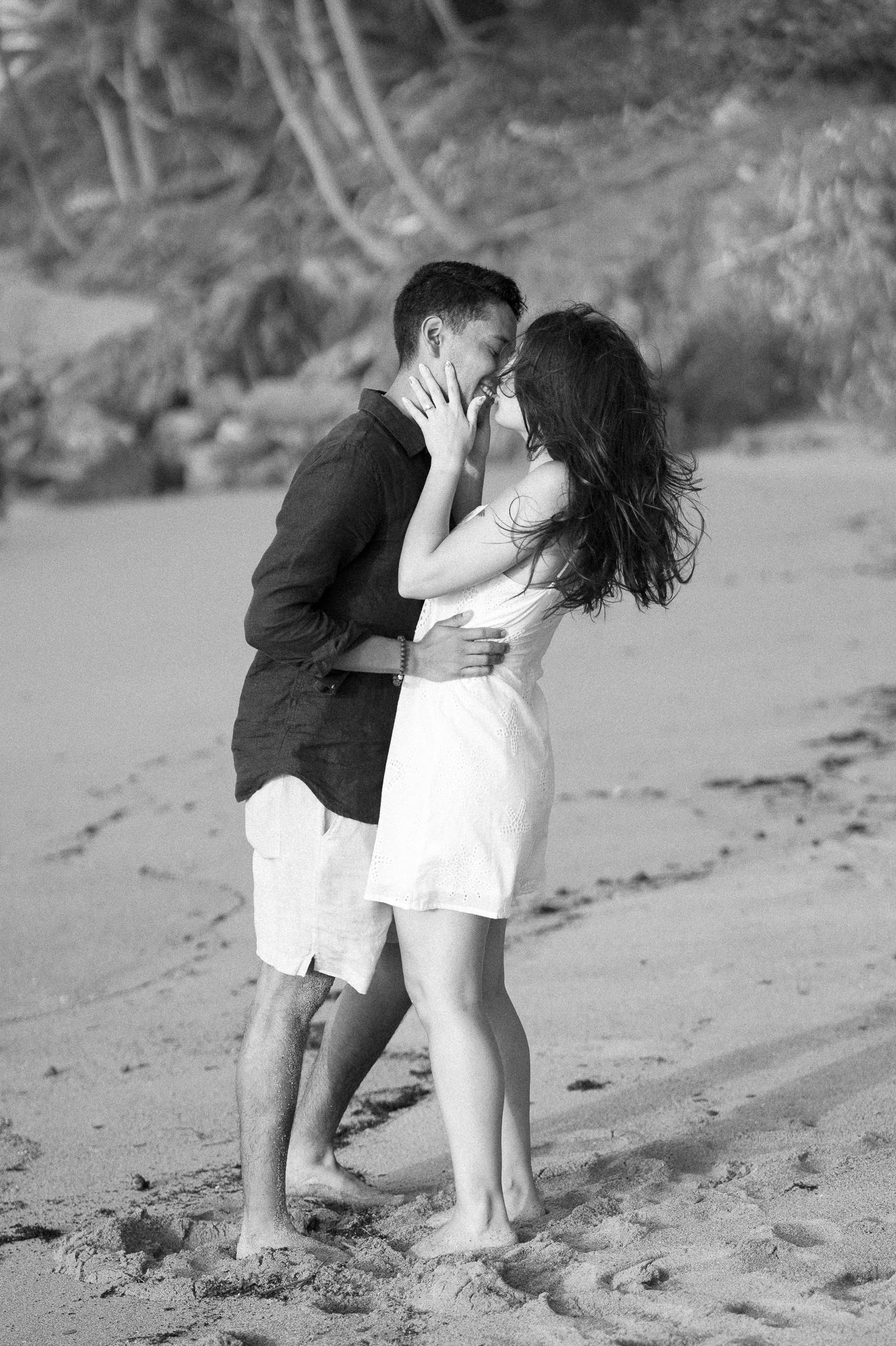 A couple shares intimate moments in black and white photos on a sandy beach.
