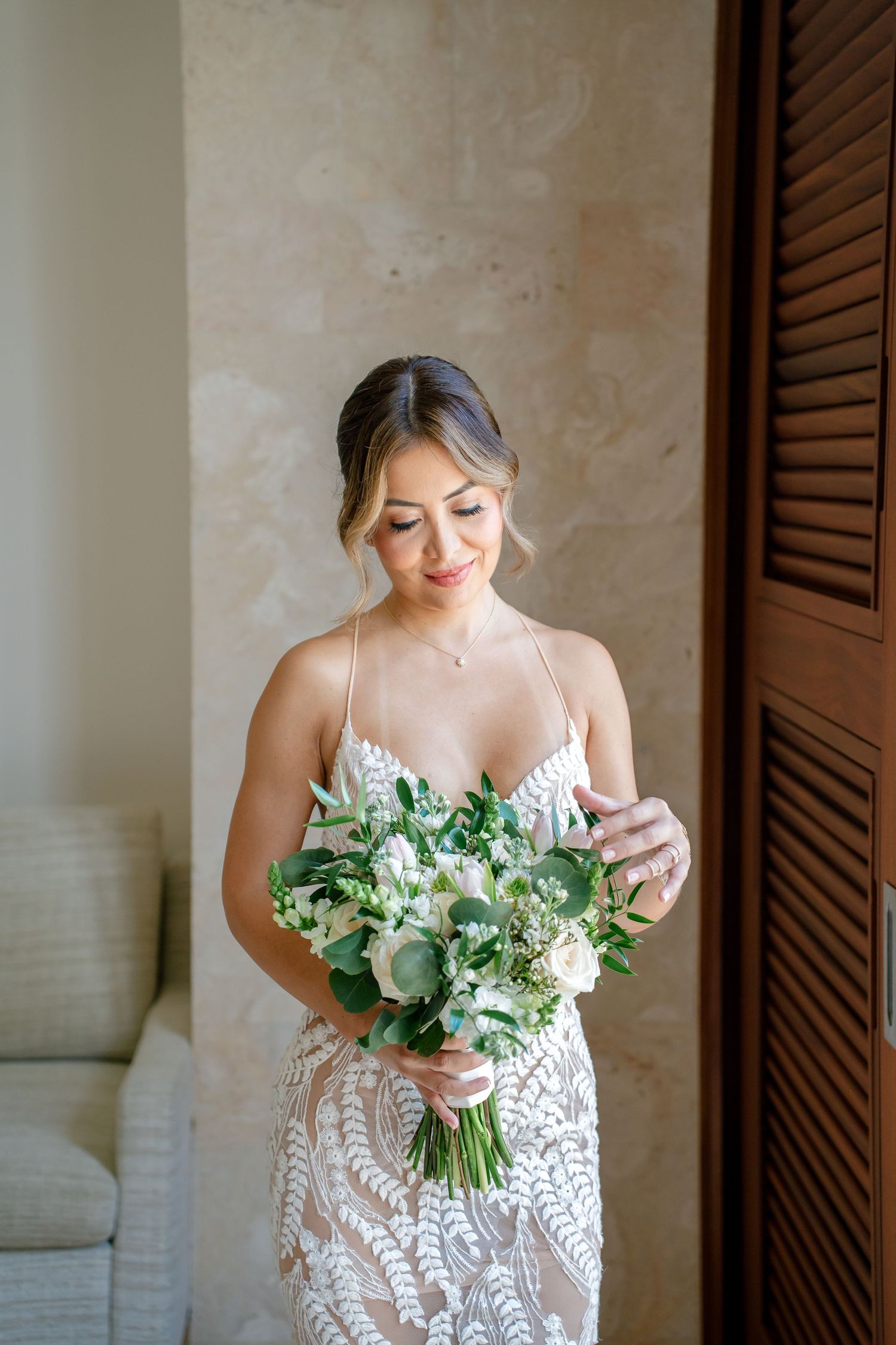 Bride in intricate lace dress holding fresh green and white wedding bouquet.