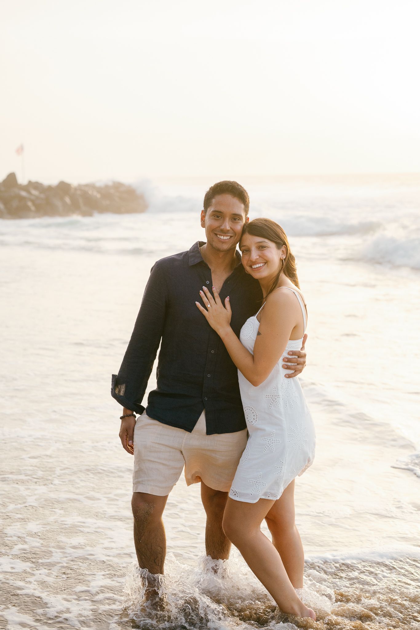 A couple shares joyful moments together while playing in the ocean waves at sunset on a sandy beach.