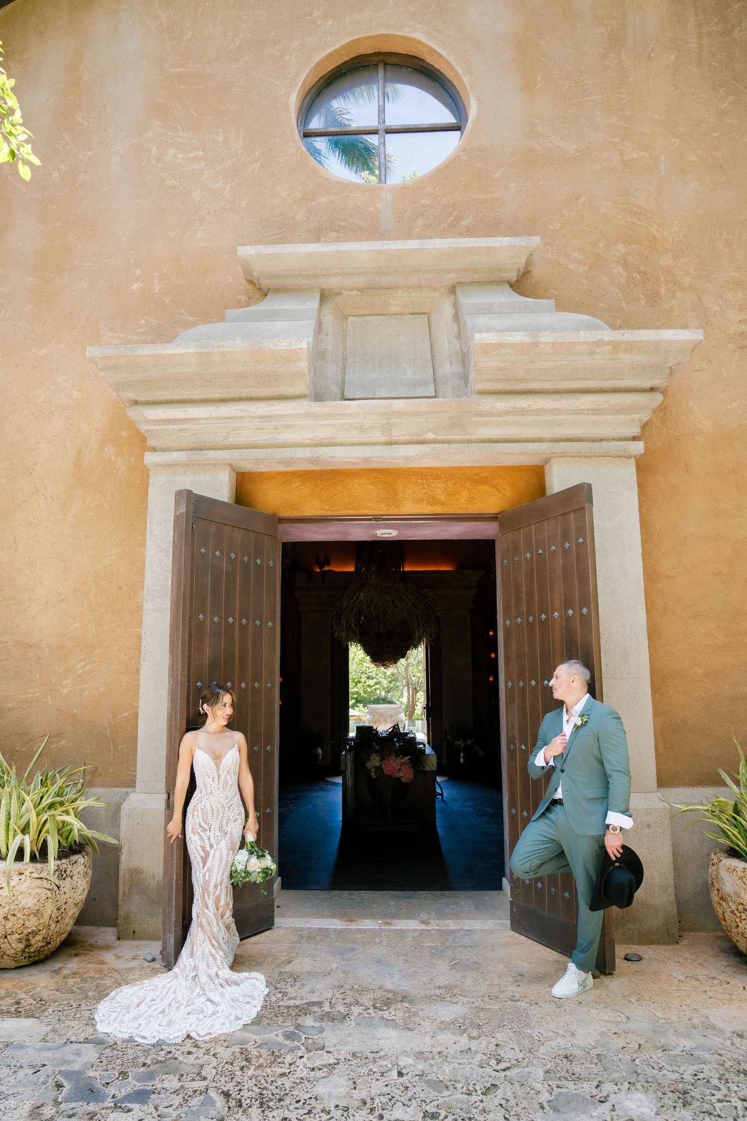 Wedding photo at rustic adobe church entrance with arched doorway.