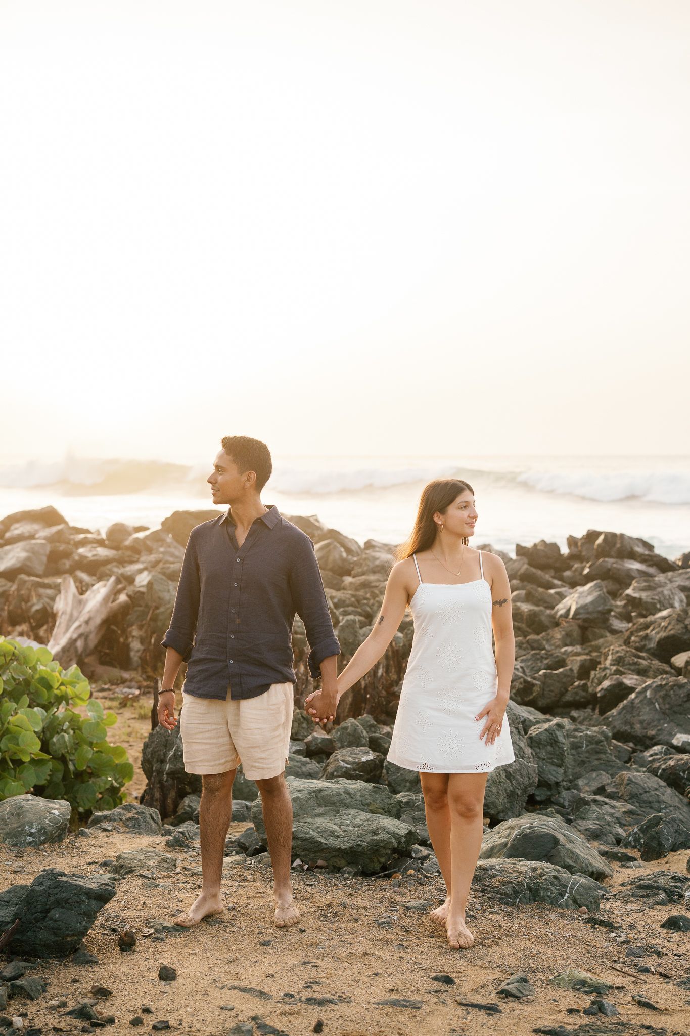 Couple walking together on a rocky beach during golden hour at sunset.