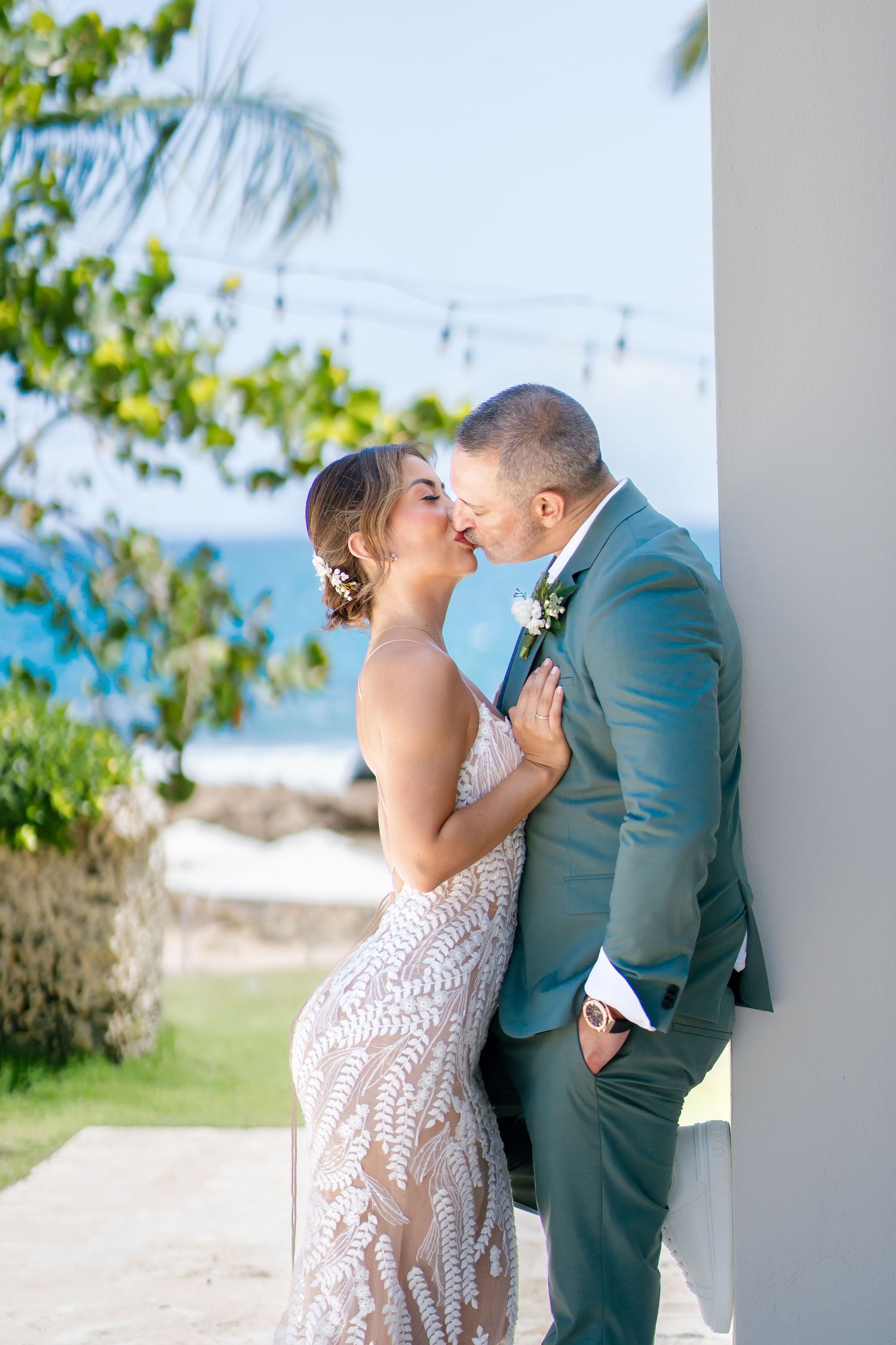 Romantic couple in wedding attire sharing intimate moment against tropical beach backdrop.