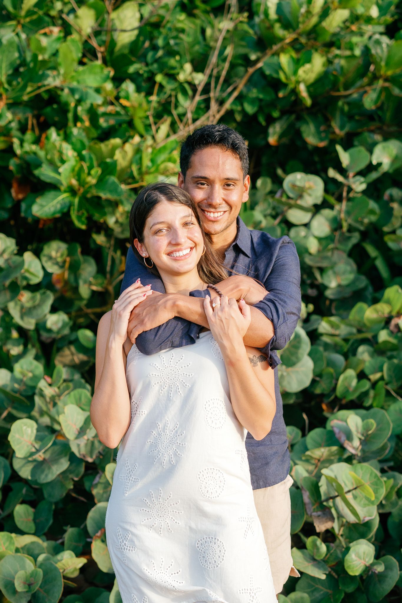 A couple embraces joyfully against a backdrop of lush green foliage in a romantic outdoor setting.