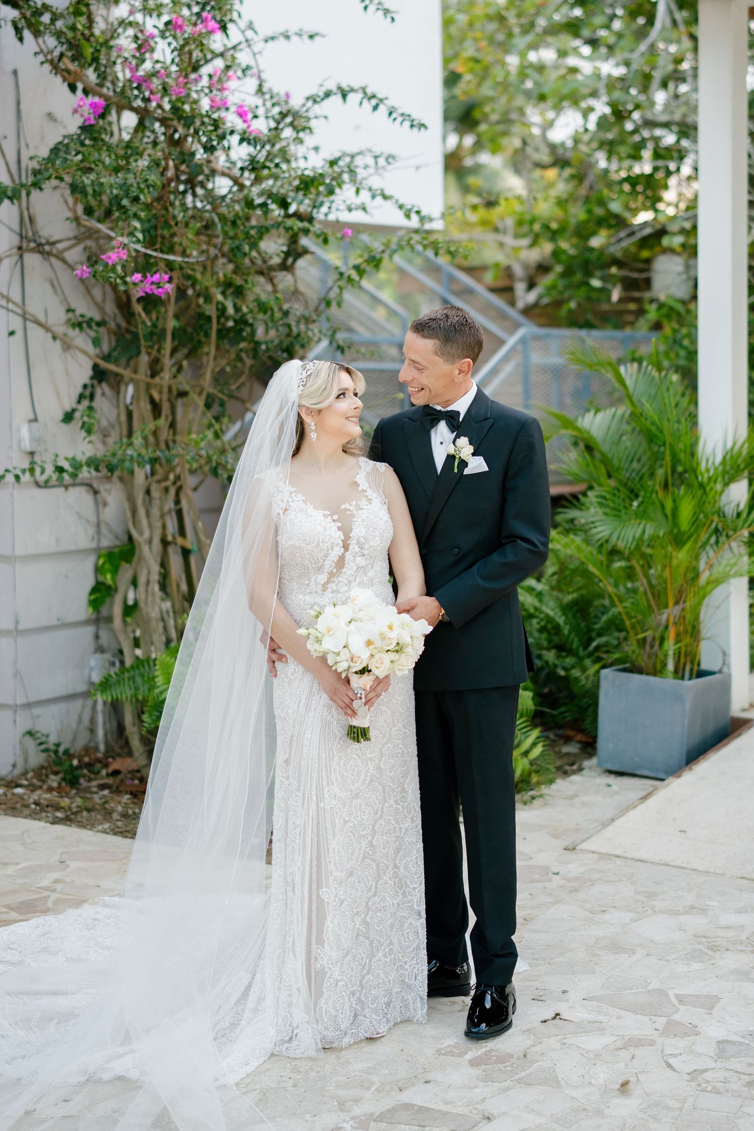 Bride and groom share a romantic moment outdoors surrounded by lush tropical greenery.