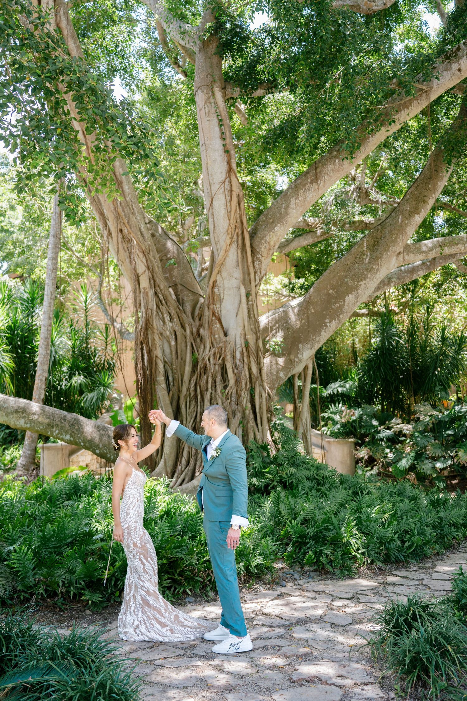 A couple captures romantic first look moments under a grand banyan tree in a lush garden setting.