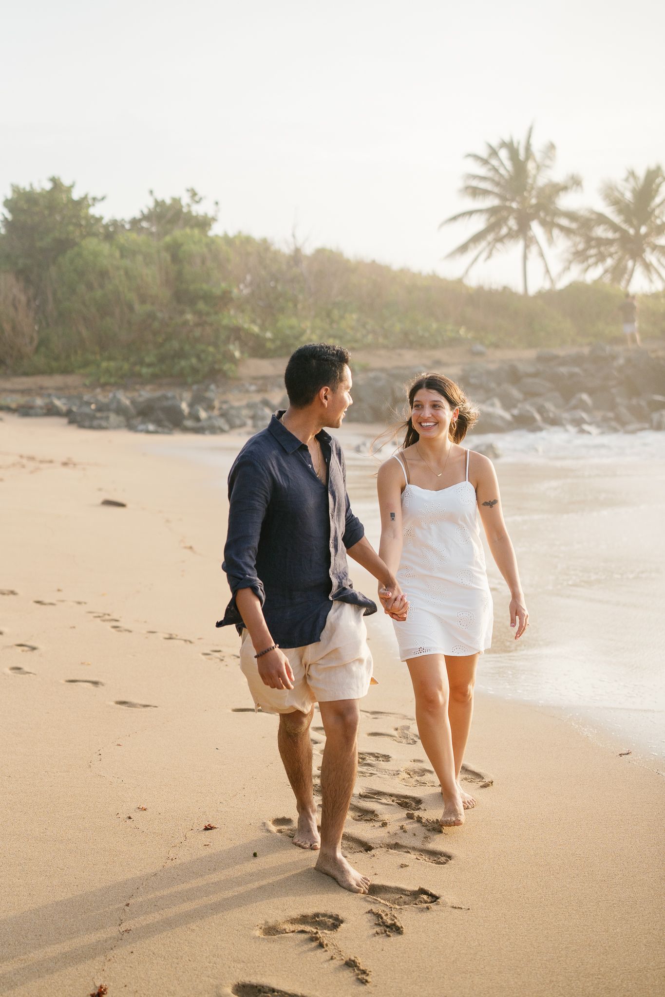 A couple walks together on a tropical beach at sunset with palm trees in the background.