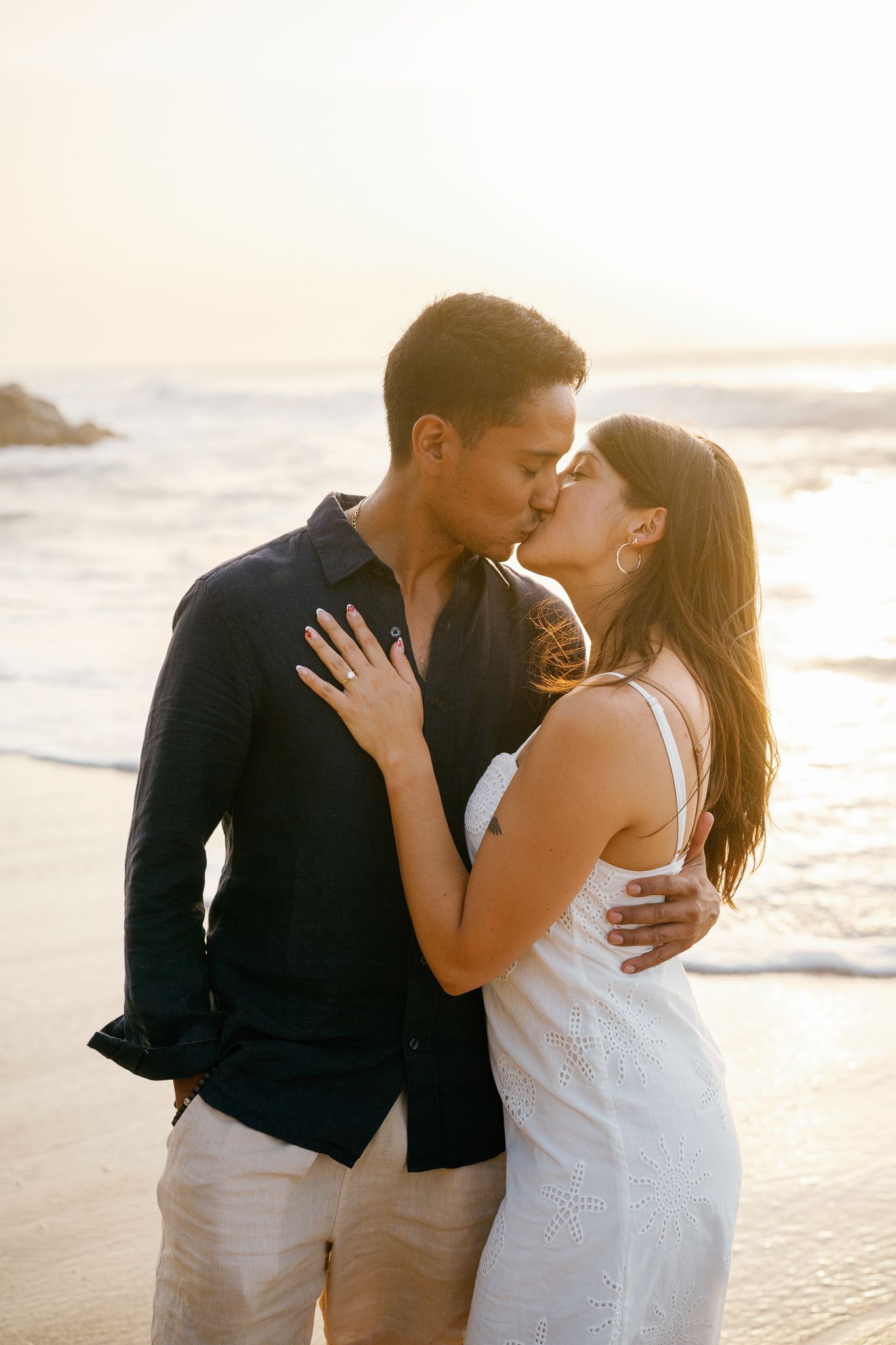 A romantic couple shares tender moments on a sunlit beach during a photo session at sunset.