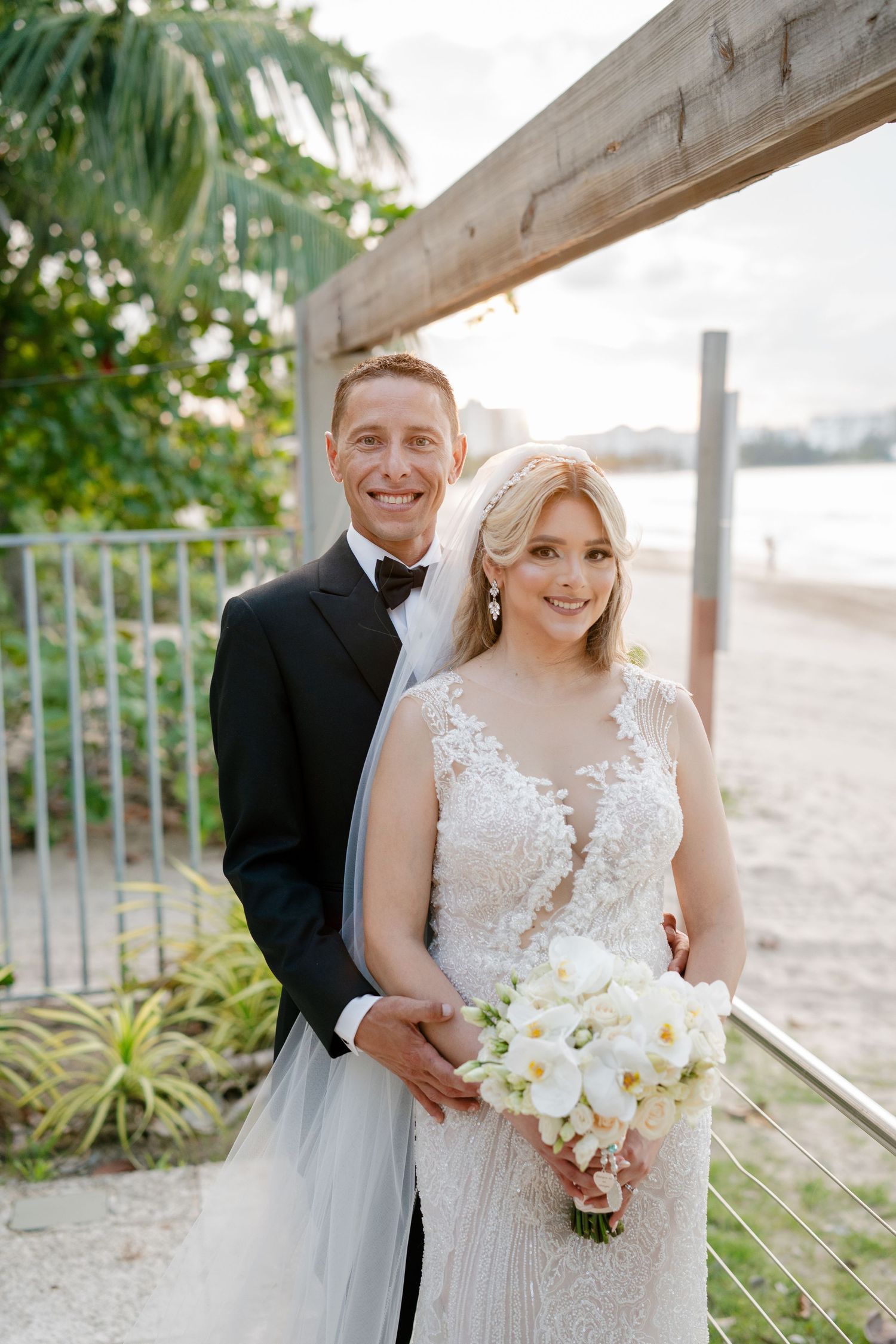 Happy bride and groom portrait on beach at golden hour with white floral bouquet.
