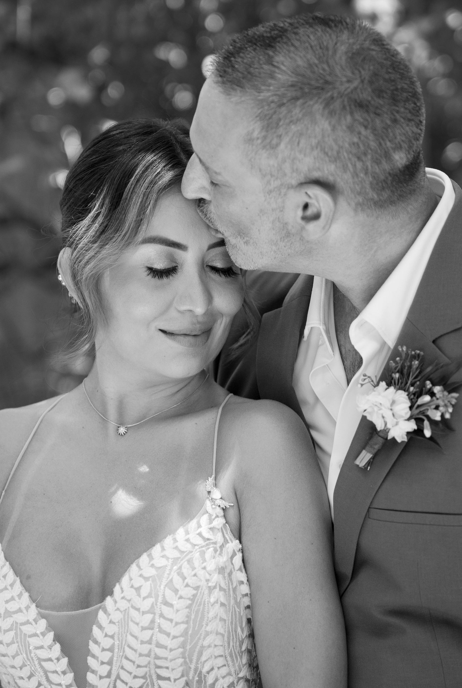 A tender black and white wedding portrait showing an intimate moment with a bride in a lace dress and groom in suit.