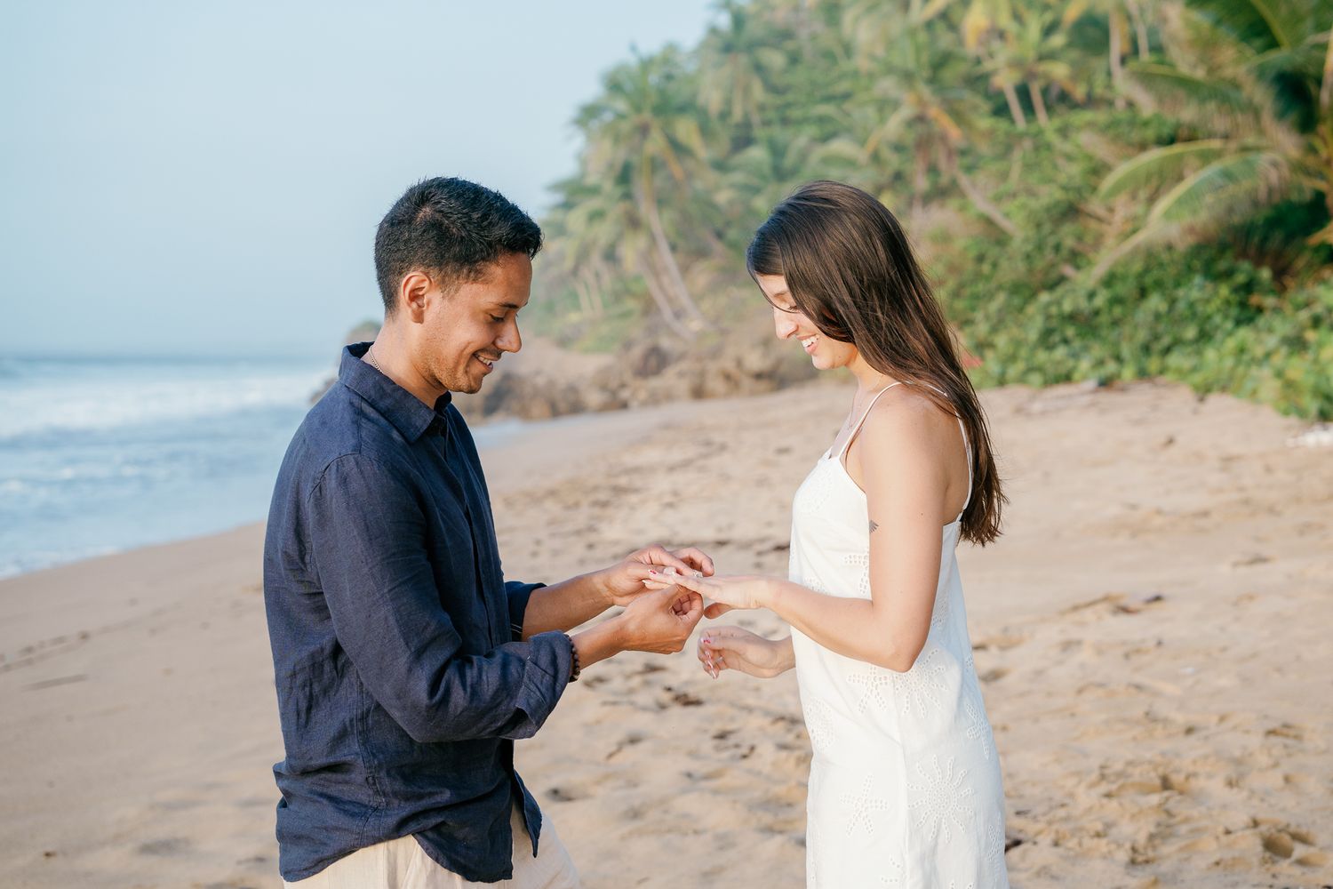 A couple shares an intimate moment during their engagement photoshoot on a scenic tropical beach.