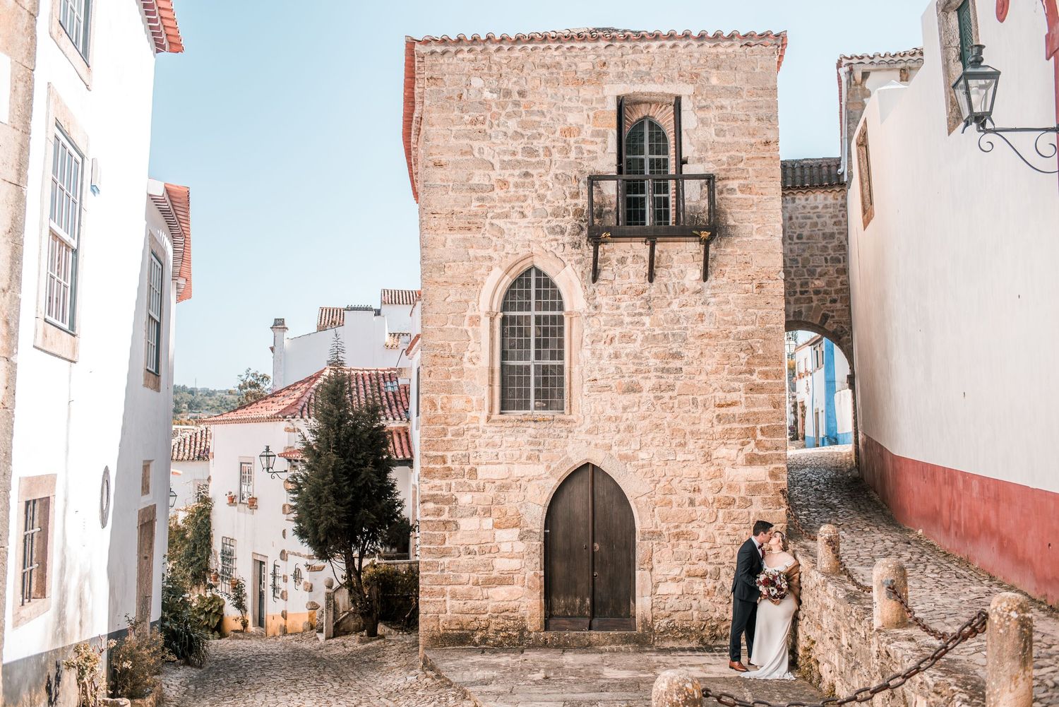 Intimate destination wedding in Óbidos, Portugal, with bride and groom walking through the medieval streets at sunset.