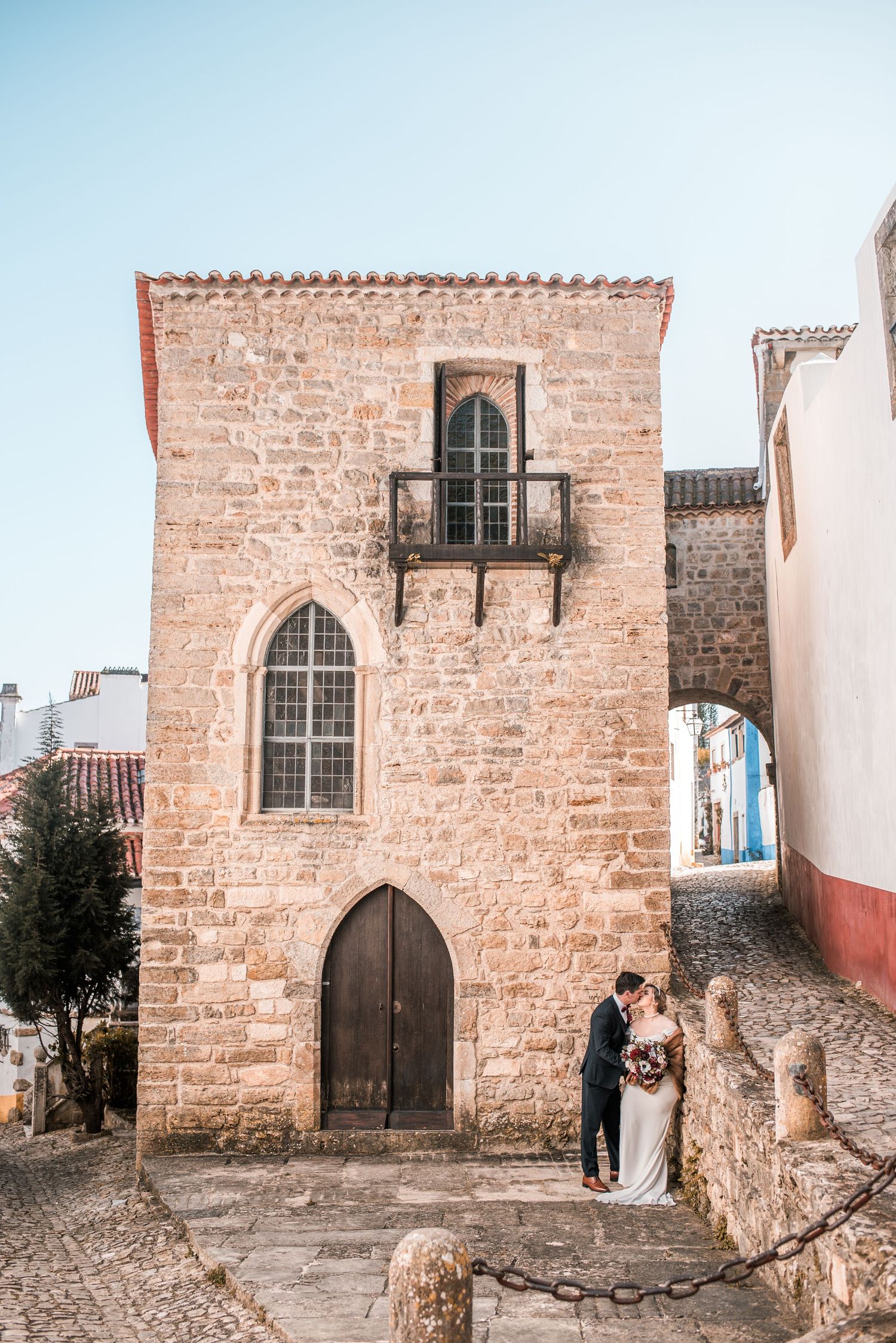 Intimate destination wedding in Óbidos, Portugal, with bride and groom walking through the medieval streets at sunset.