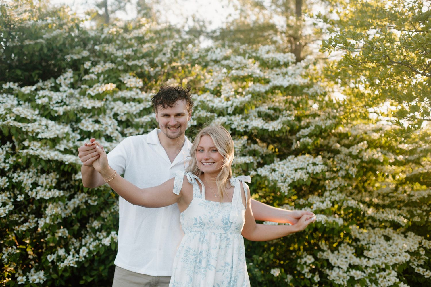Couple smiling in front of flowering bush during their engagement session at Millenium Park in Grand Rapids, MI.