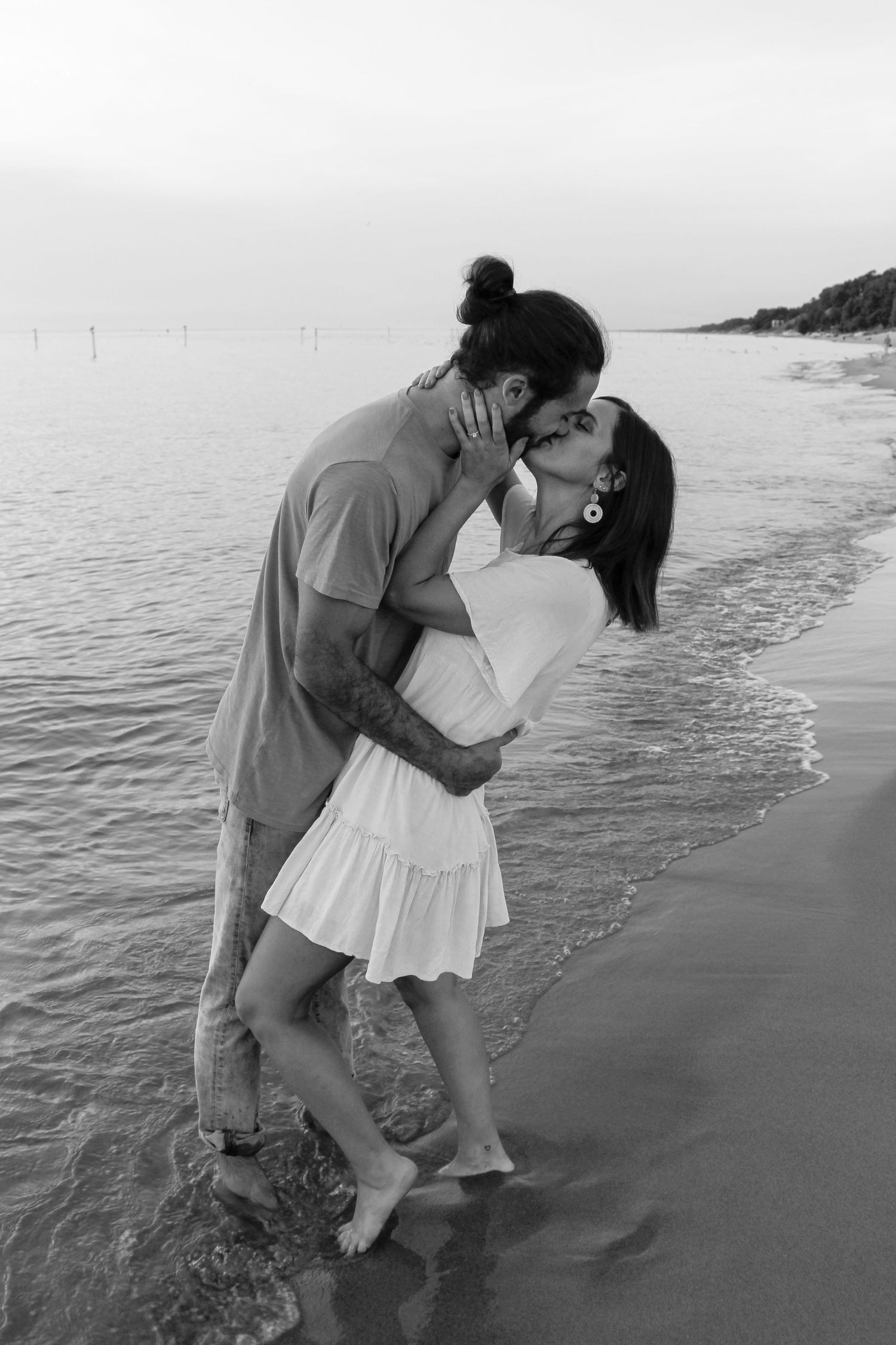 Couple embracing and kissing during their engagement session in Holland, MI at sunset, in black and white.