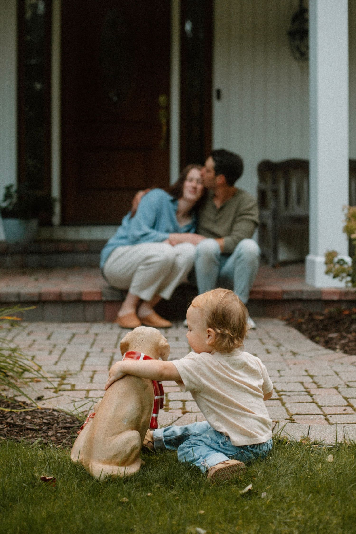 Couple embracing on their front porch while their son looks on during their outdoor family session in West Michigan.