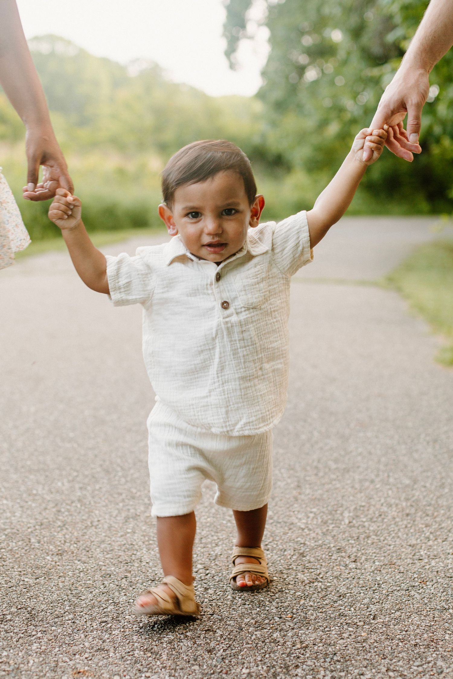 Young boy holding his parent's hands while walking during their outdoor family session at Grand Ravines Park.