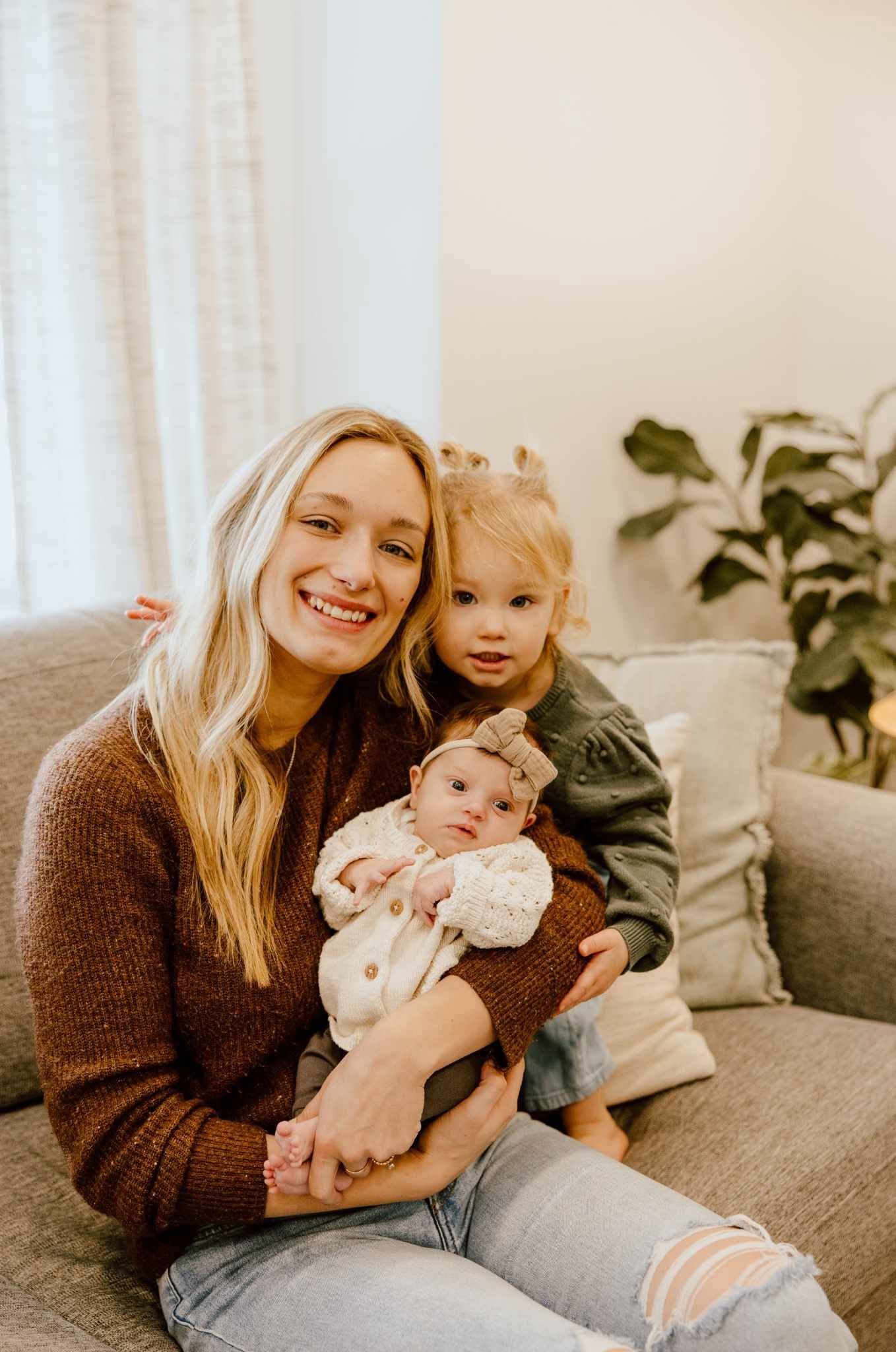 Eden with her two daughters sitting on the couch during at home newborn session.