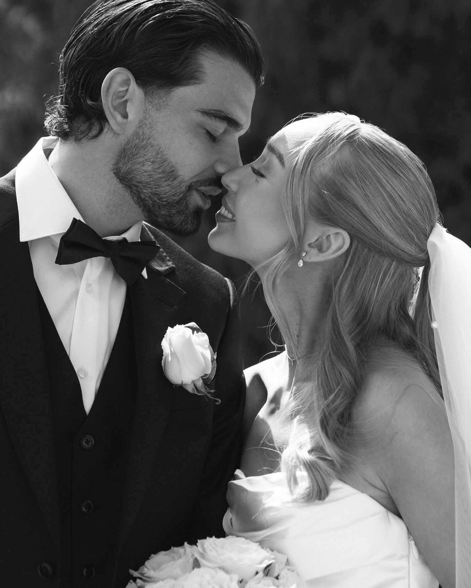 Black and white wedding photo of bride and groom sharing a romantic kiss, bride holding bouquet.