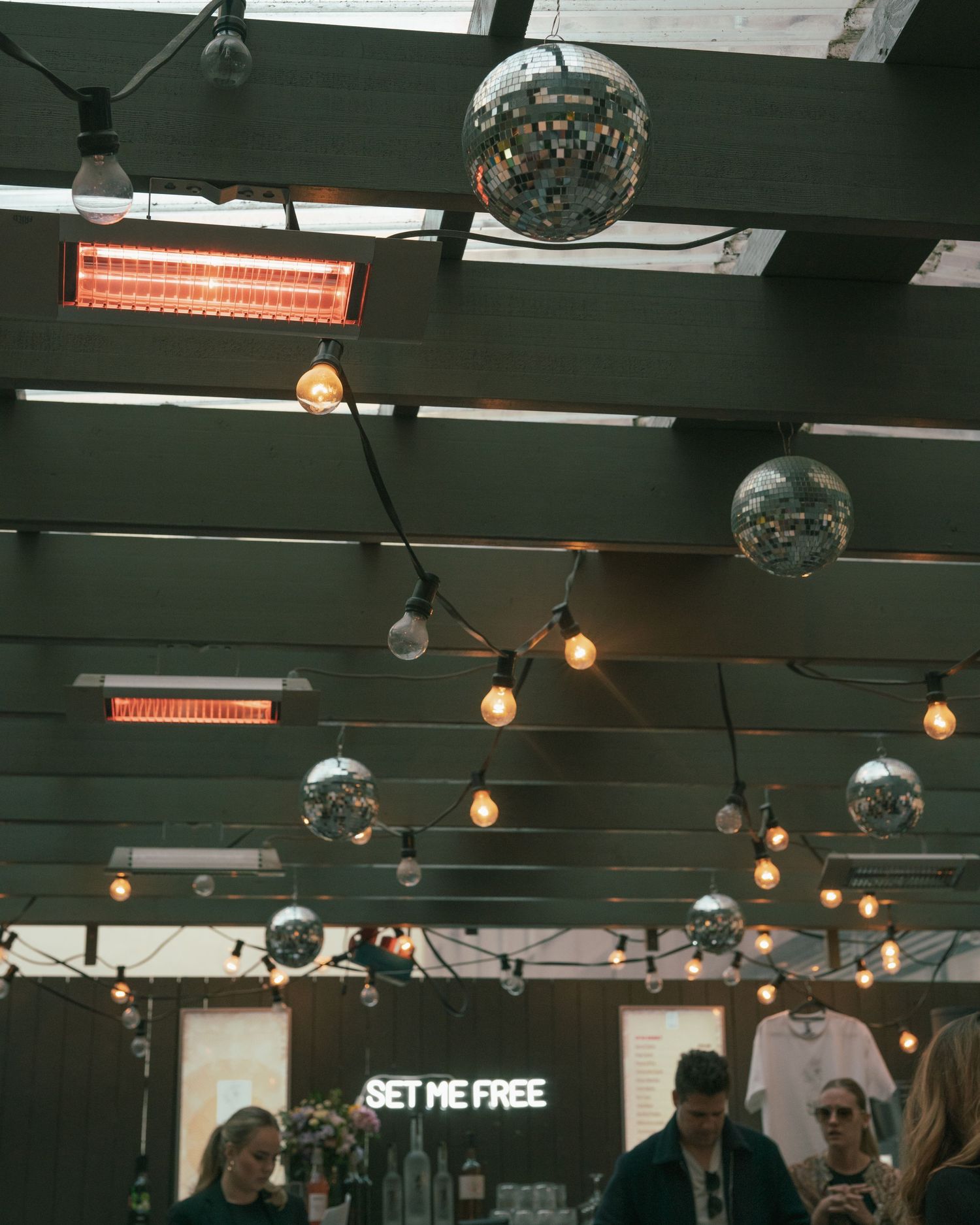 Disco balls and string lights hang from dark ceiling beams above a retail space with neon signage.