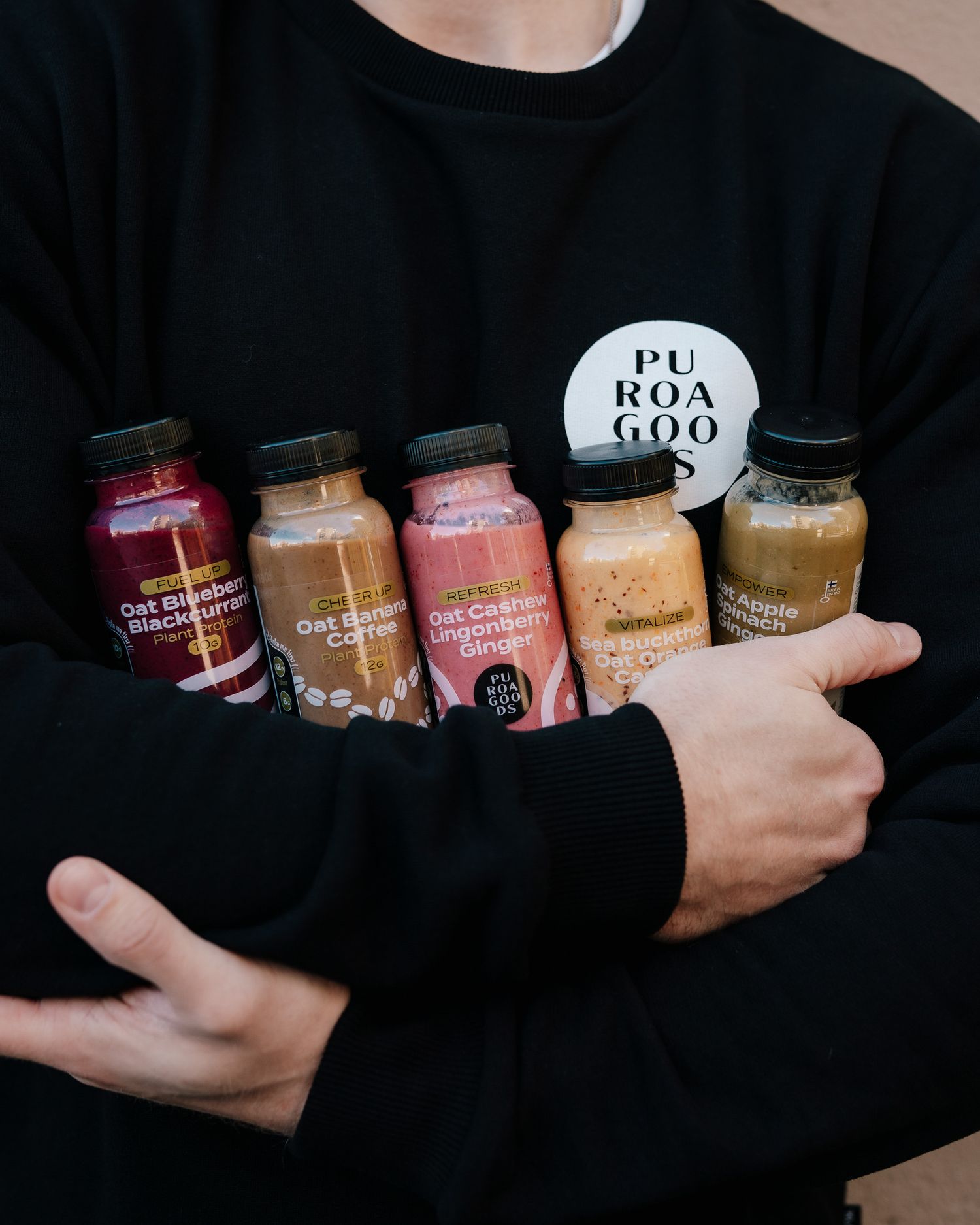 Person in black sweater holding assorted colorful smoothie bottles with PURAGOGO branding.