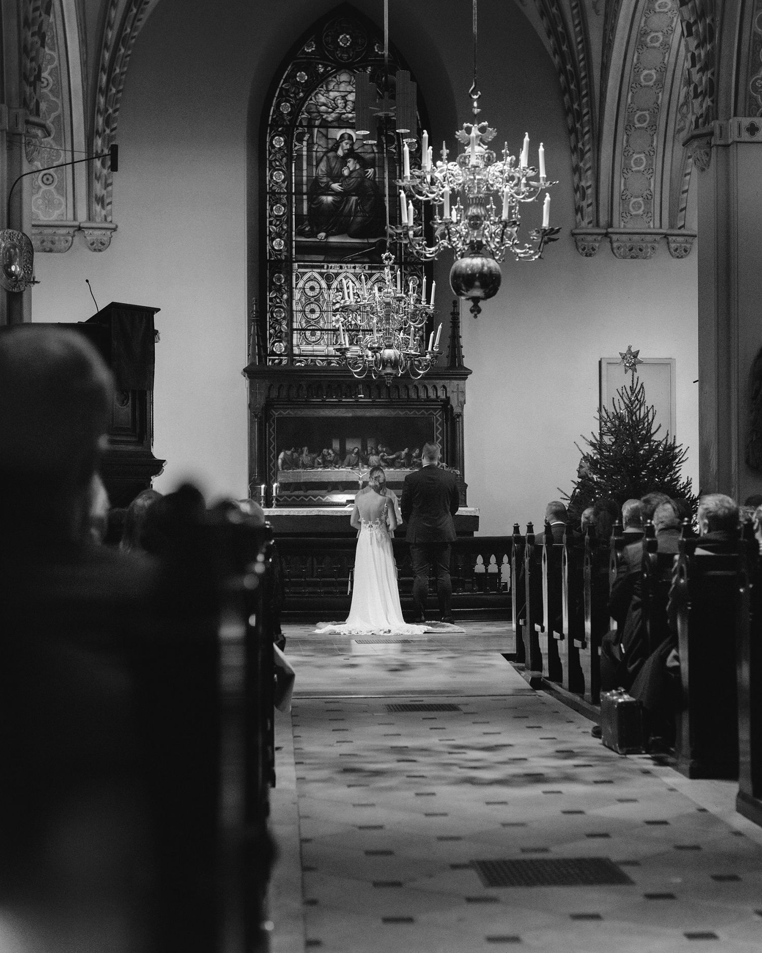 Black and white photograph of a church interior with an ornate chandelier and rows of pews during a ceremony.