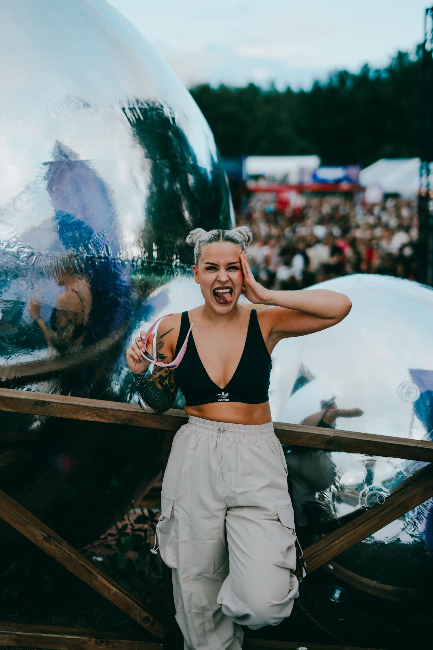Festival goer in black crop top and white cargo pants poses in front of a large crowd during an outdoor summer event.
