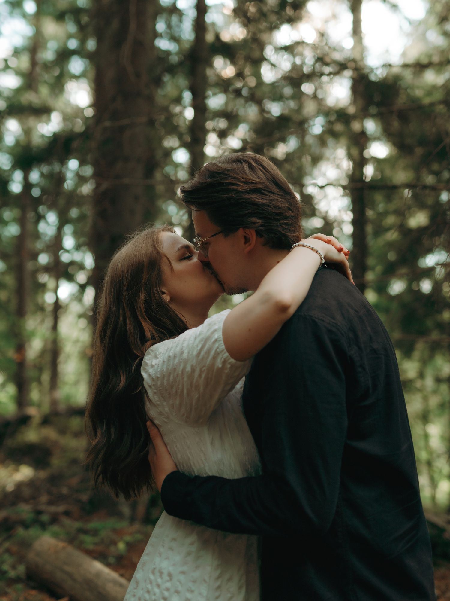 A romantic moment shared between two people embracing and kissing in a sunlit forest.