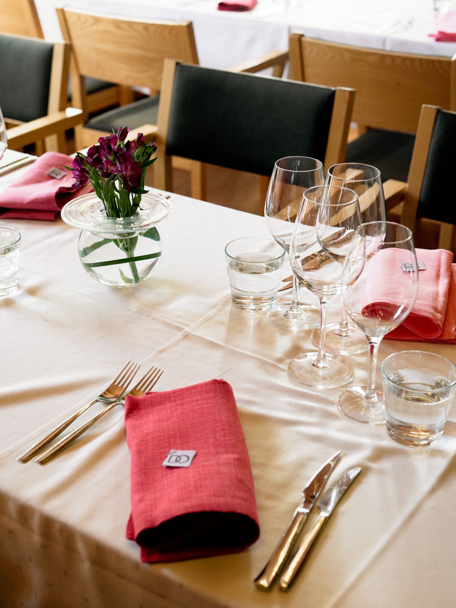 Elegant restaurant table setting with pink linen napkins, gold cutlery, crystal wine glasses, and a floral centerpiece.