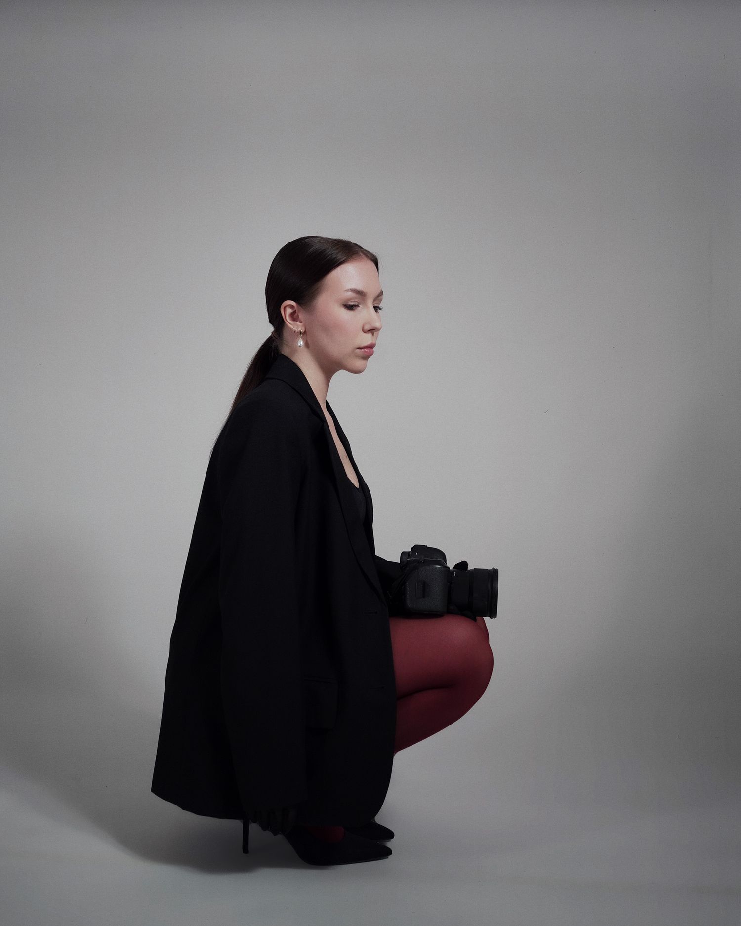 Figure in a black coat poses against grey background with red and black accessories.