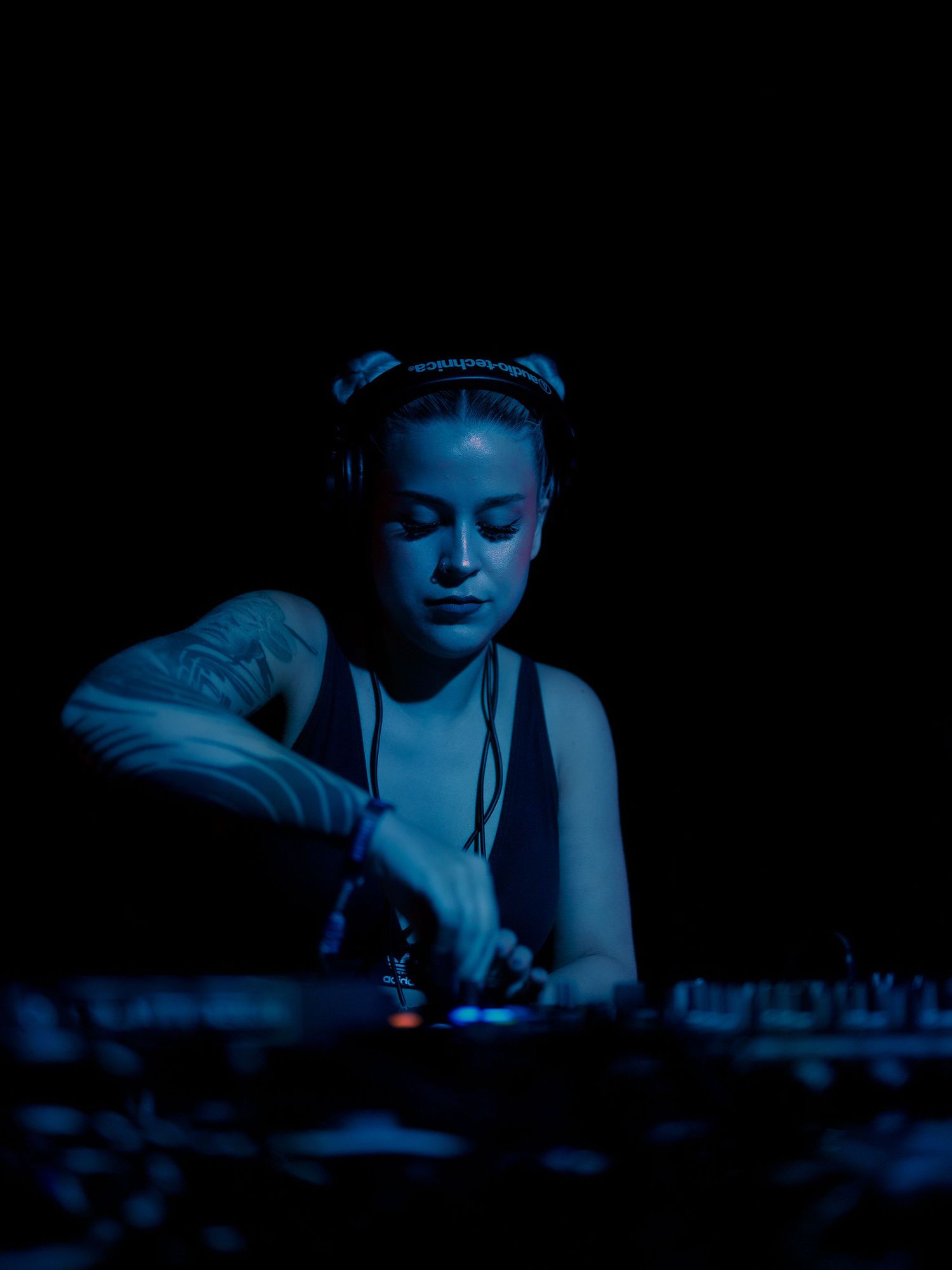 A DJ performs at night under dramatic blue lighting while concentrating on the mixing equipment.