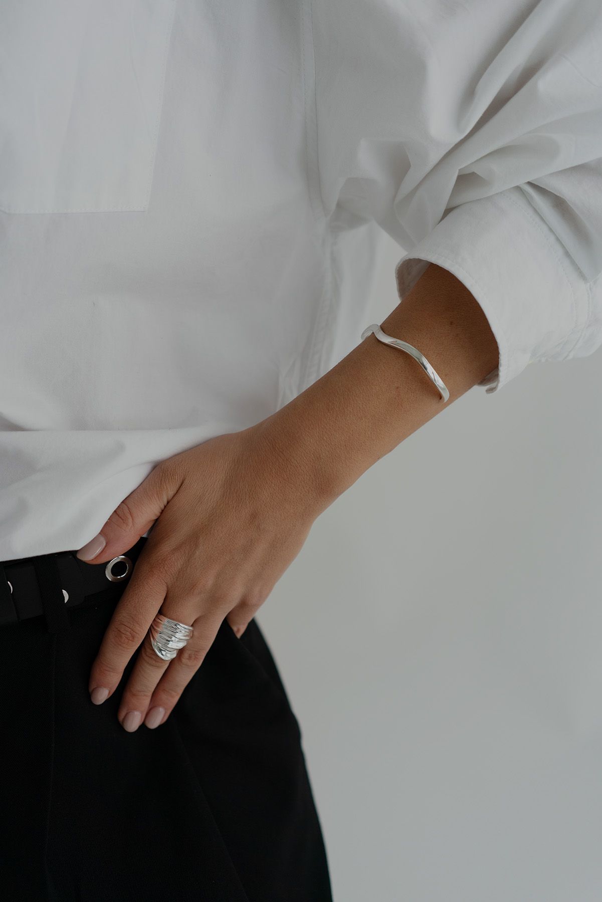 Close-up of hand wearing white bracelet and statement ring with white shirt sleeve.