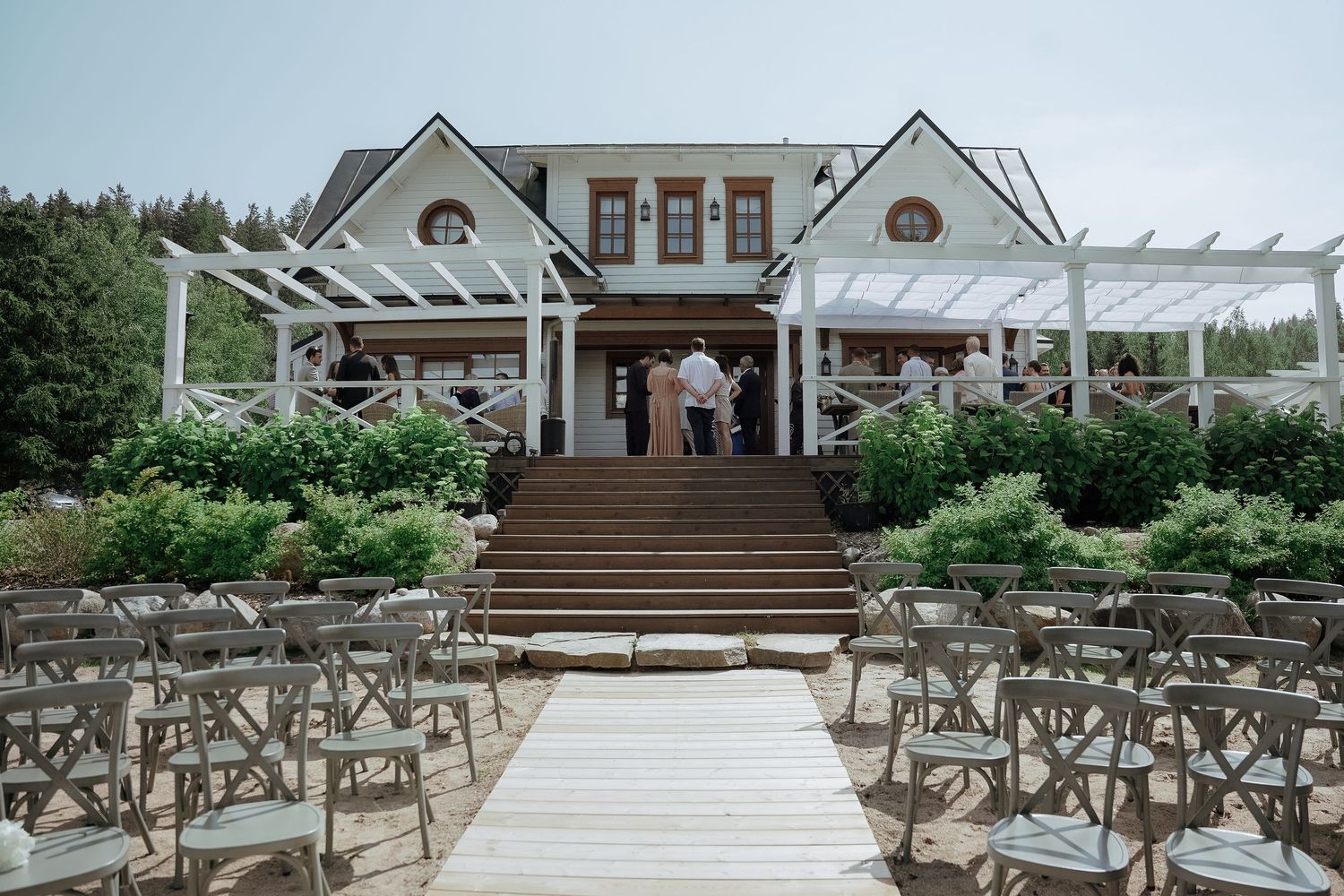 Elegant white estate house with pergolas and rustic wooden chairs set up for an outdoor wedding ceremony.