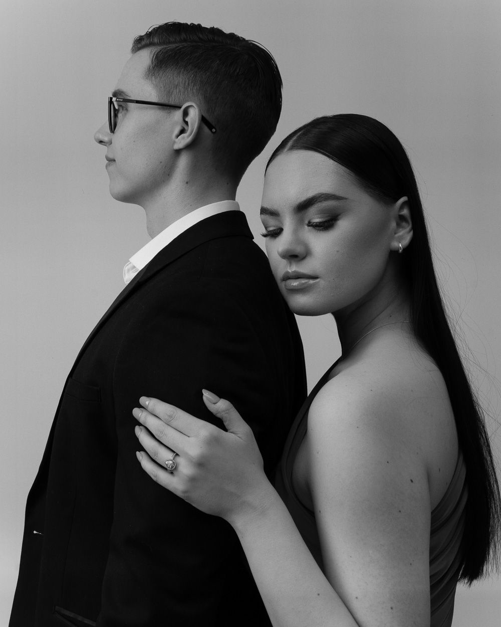 A black and white artistic portrait of a couple in formal wear, showing an intimate back-facing pose.