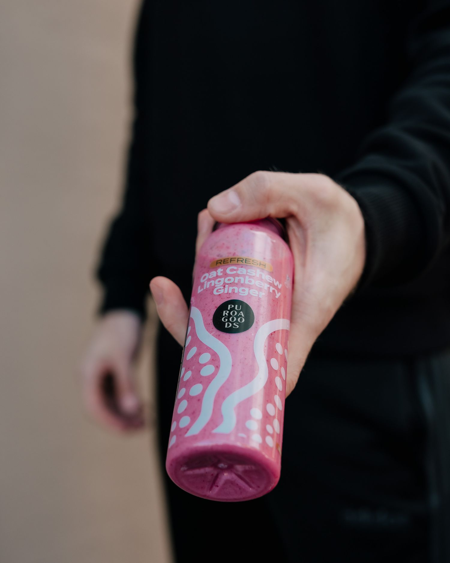 Hand holding a pink canned beverage with swirling designs against a neutral background.