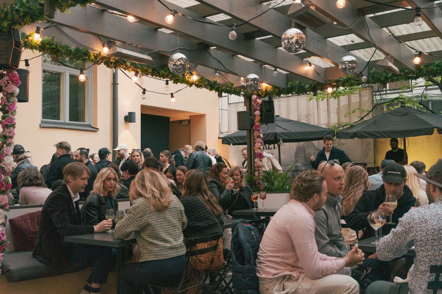 Crowded outdoor patio dining area with string lights and umbrellas creating a cozy evening atmosphere.