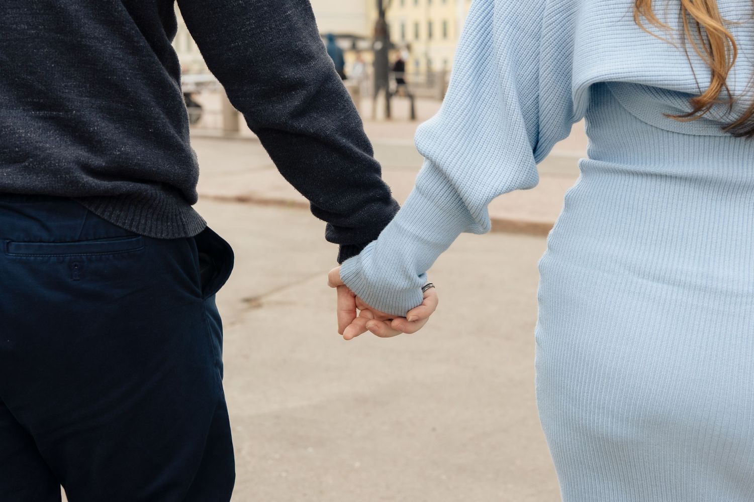 Couple holding hands while walking together outdoors, wearing casual blue and gray clothing.