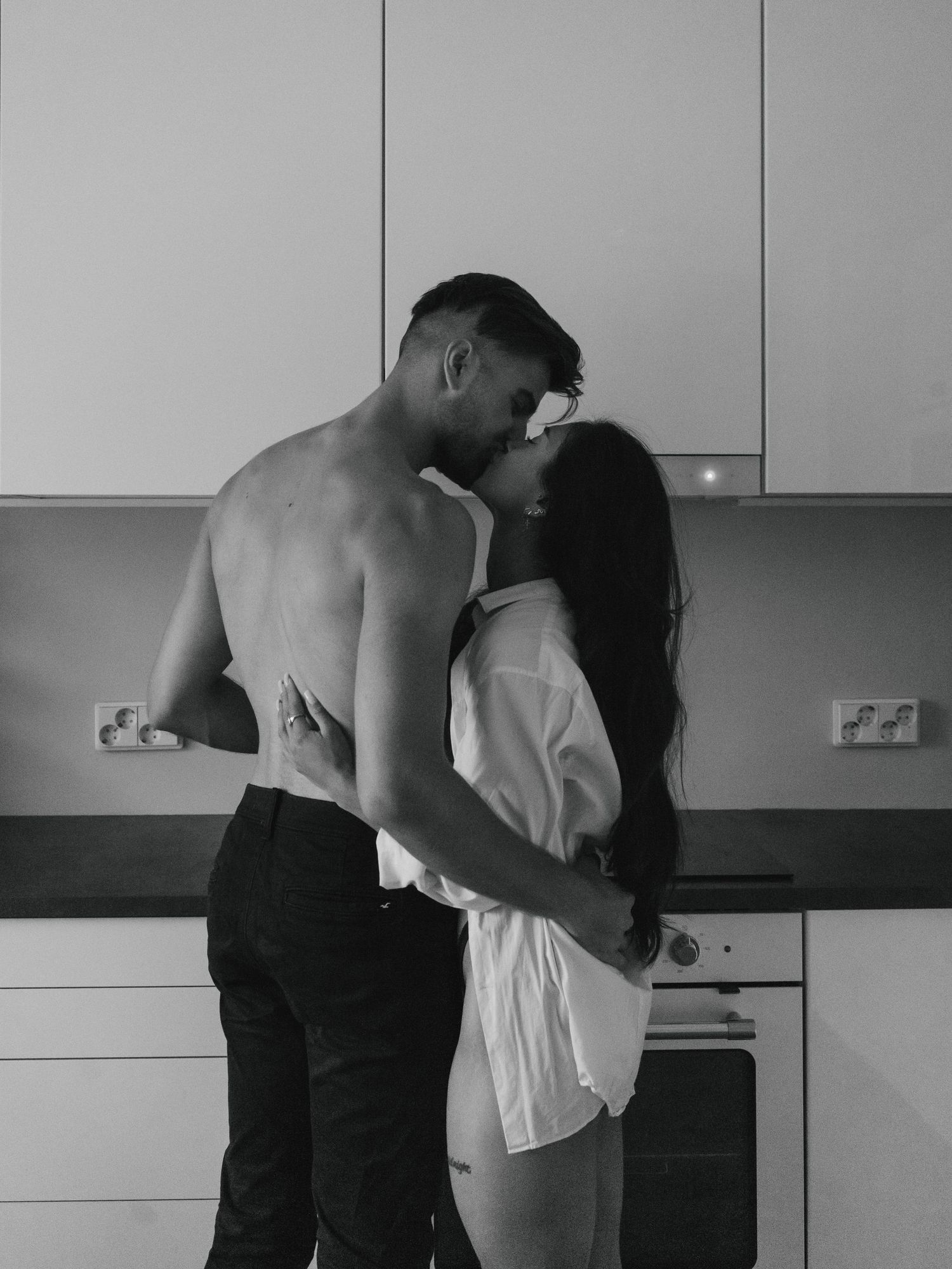 A tender black and white romantic moment shared between a couple embracing in a modern minimalist kitchen.