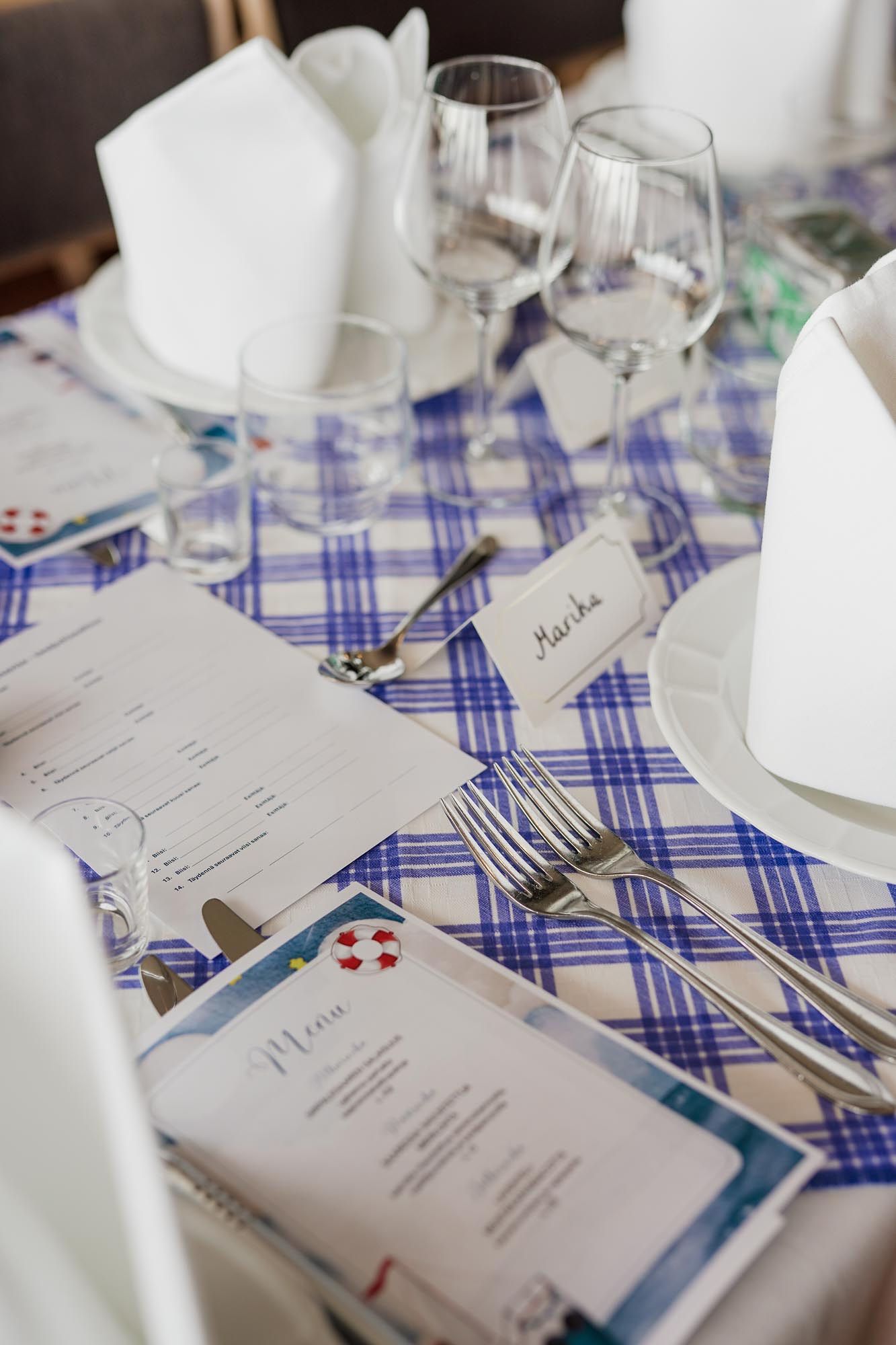 Elegant nautical-themed table setting with blue plaid tablecloth, menu cards, wine glasses, and silverware for a formal event.