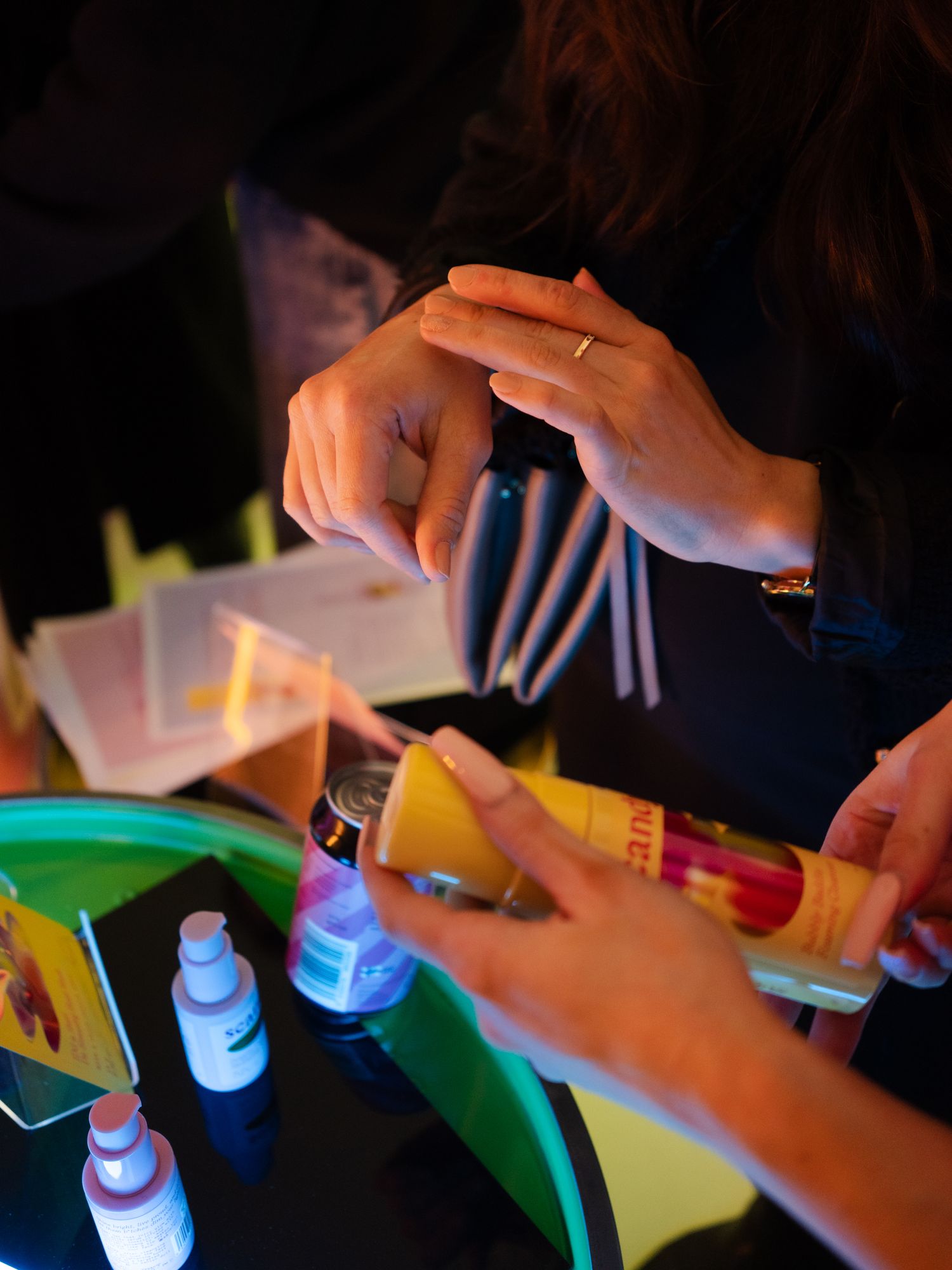 Hands work with craft supplies and small bottles on a green tray in warm lighting.