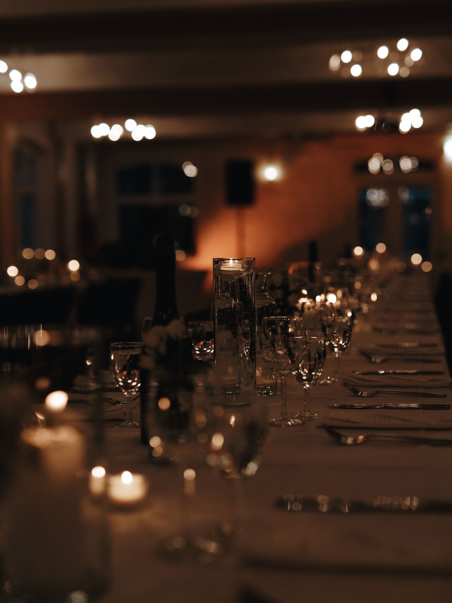 A long dining table set for a formal dinner with candlelight and glassware in a dimly lit elegant restaurant setting.
