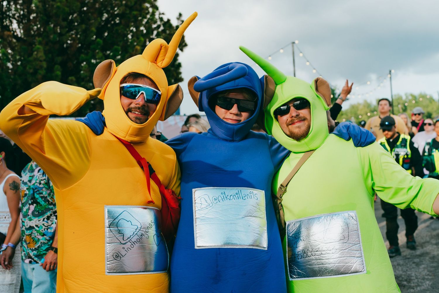 Colorful group in yellow, blue and green costume outfits posing outdoors with silly expressions and sunglasses.