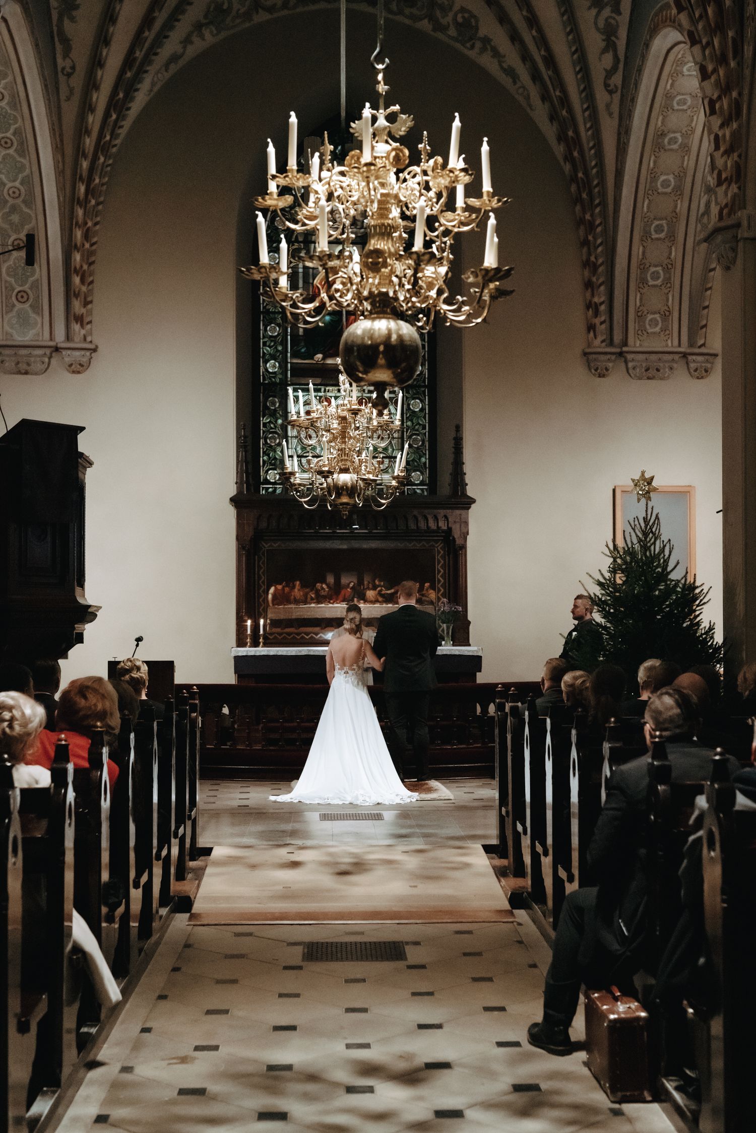Elegant church interior with ornate chandelier and white floral arrangements during a wedding ceremony.
