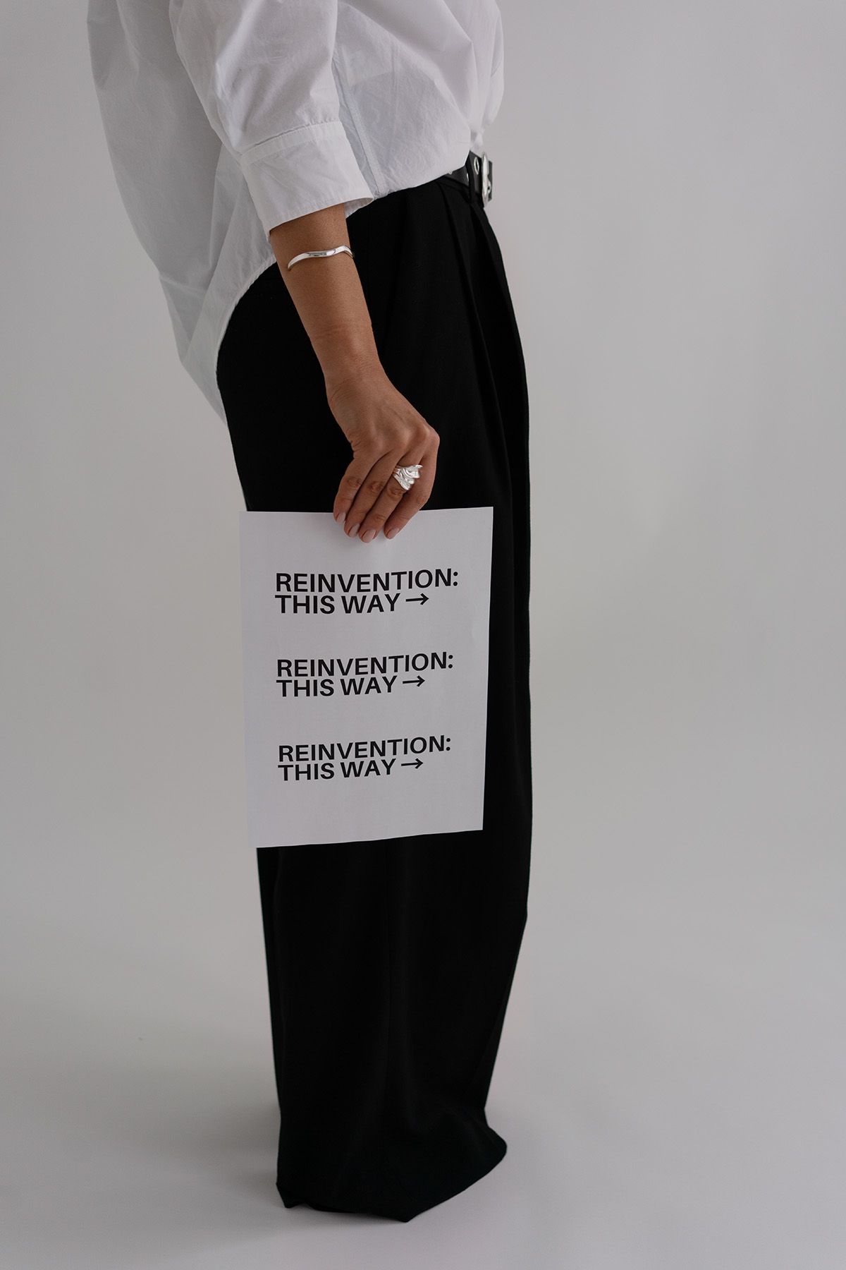 Minimalist fashion photo showing black pants with 'Reinvention' text detail.