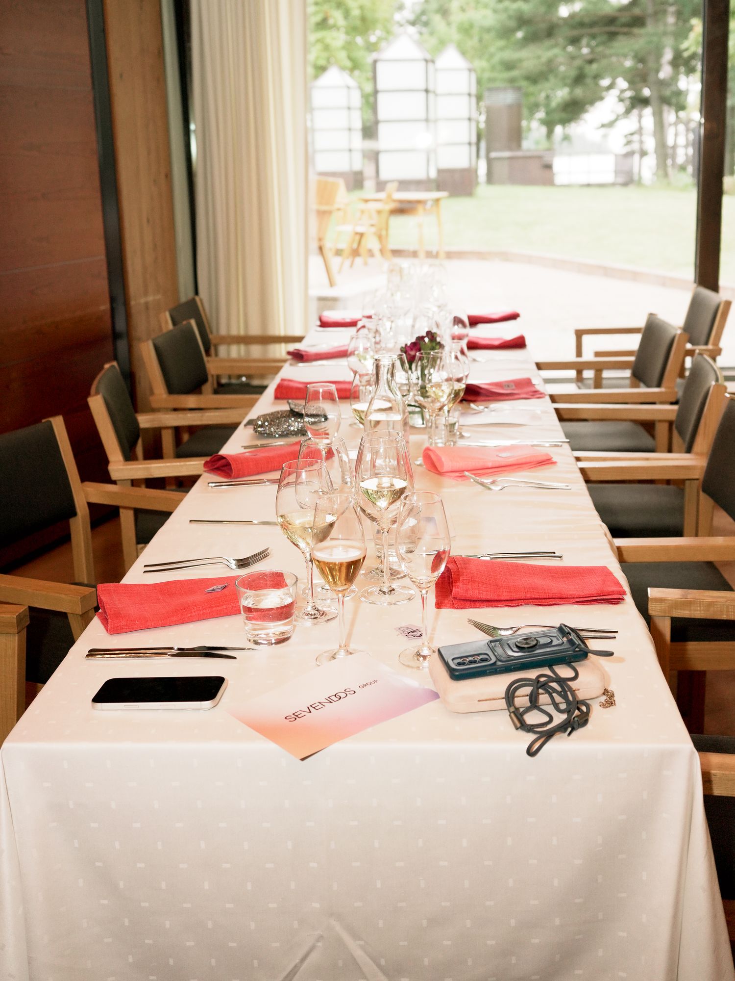 Elegant dining table set with red napkins, wine glasses, and white tablecloth in a modern restaurant setting.